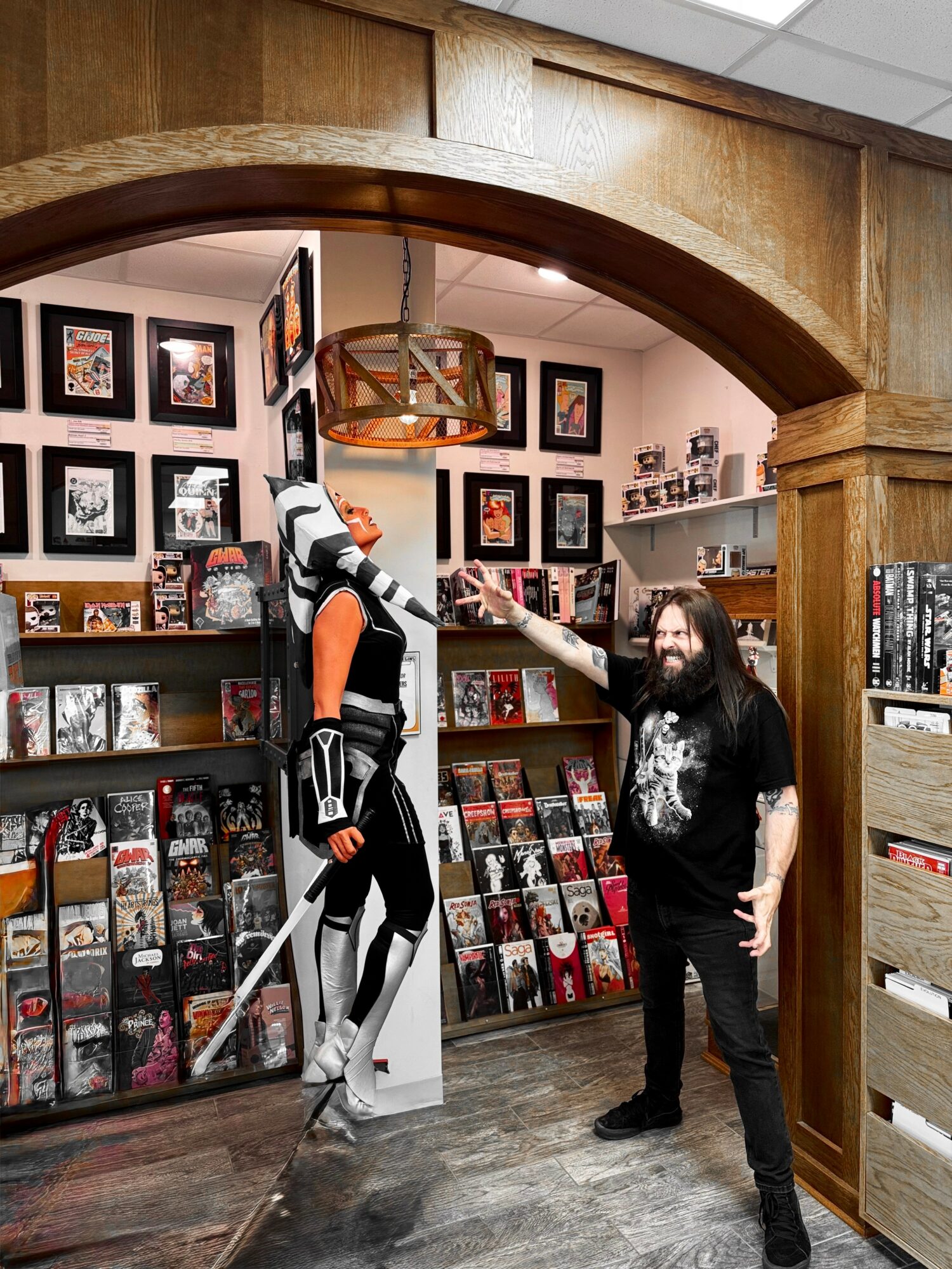 Person in a costume with a sword and armor standing inside a bookstore, talking to a man with long hair and glasses, bookshelves behind them.