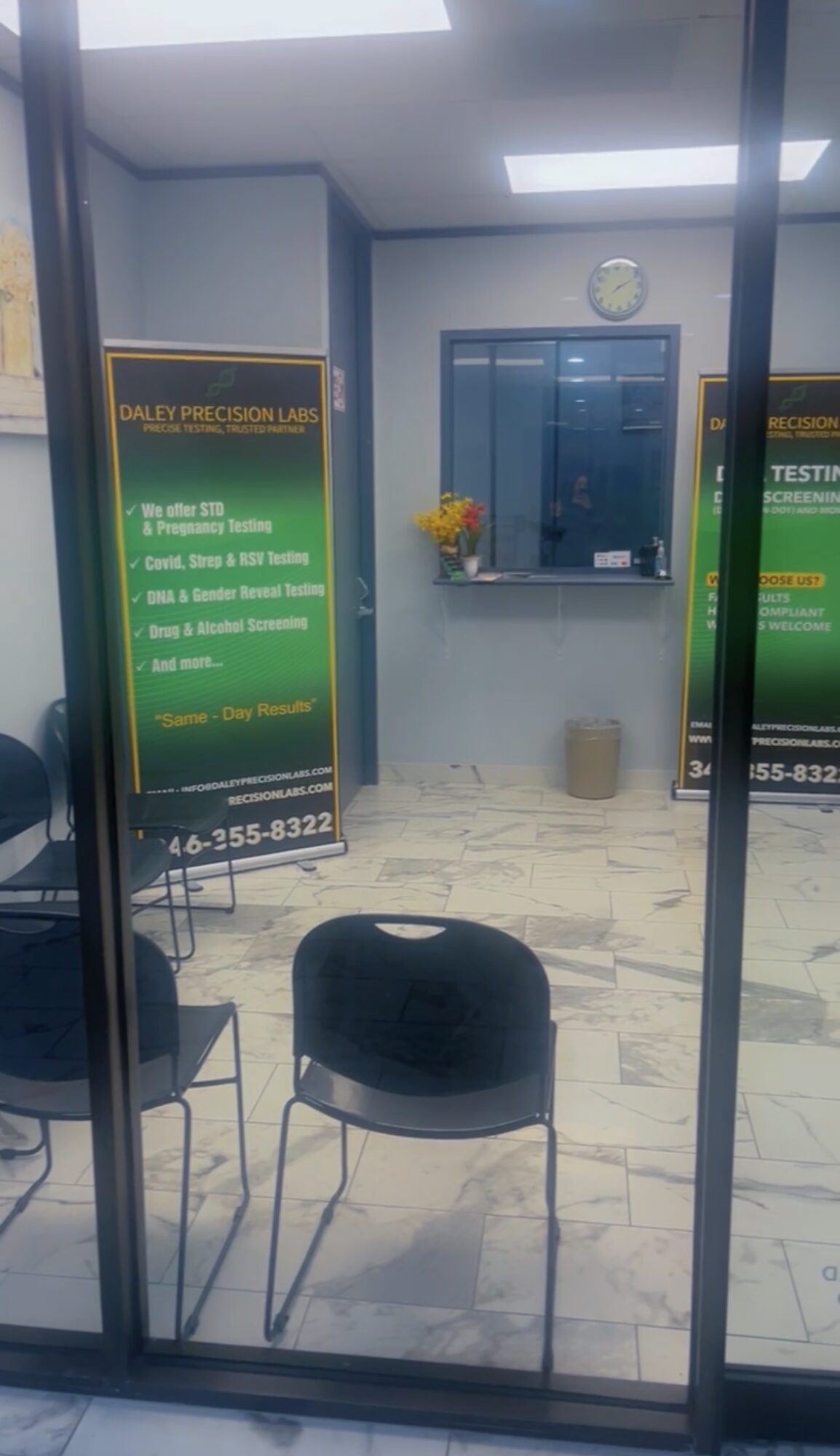 View through glass door showing chairs, a wall clock, a window, and informational signs inside a room.