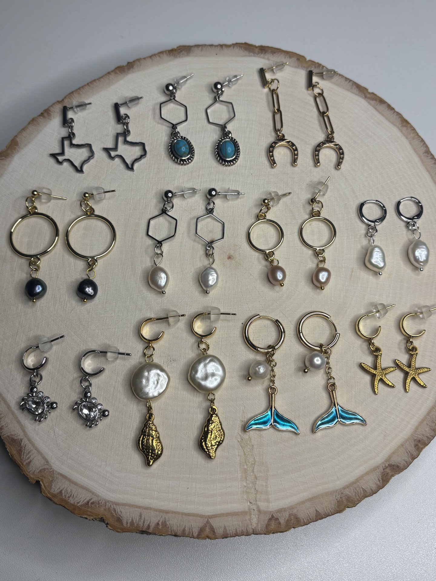 Collection of earrings arranged on a round wooden surface, including hoops, dangles, and studs in various styles and colors.