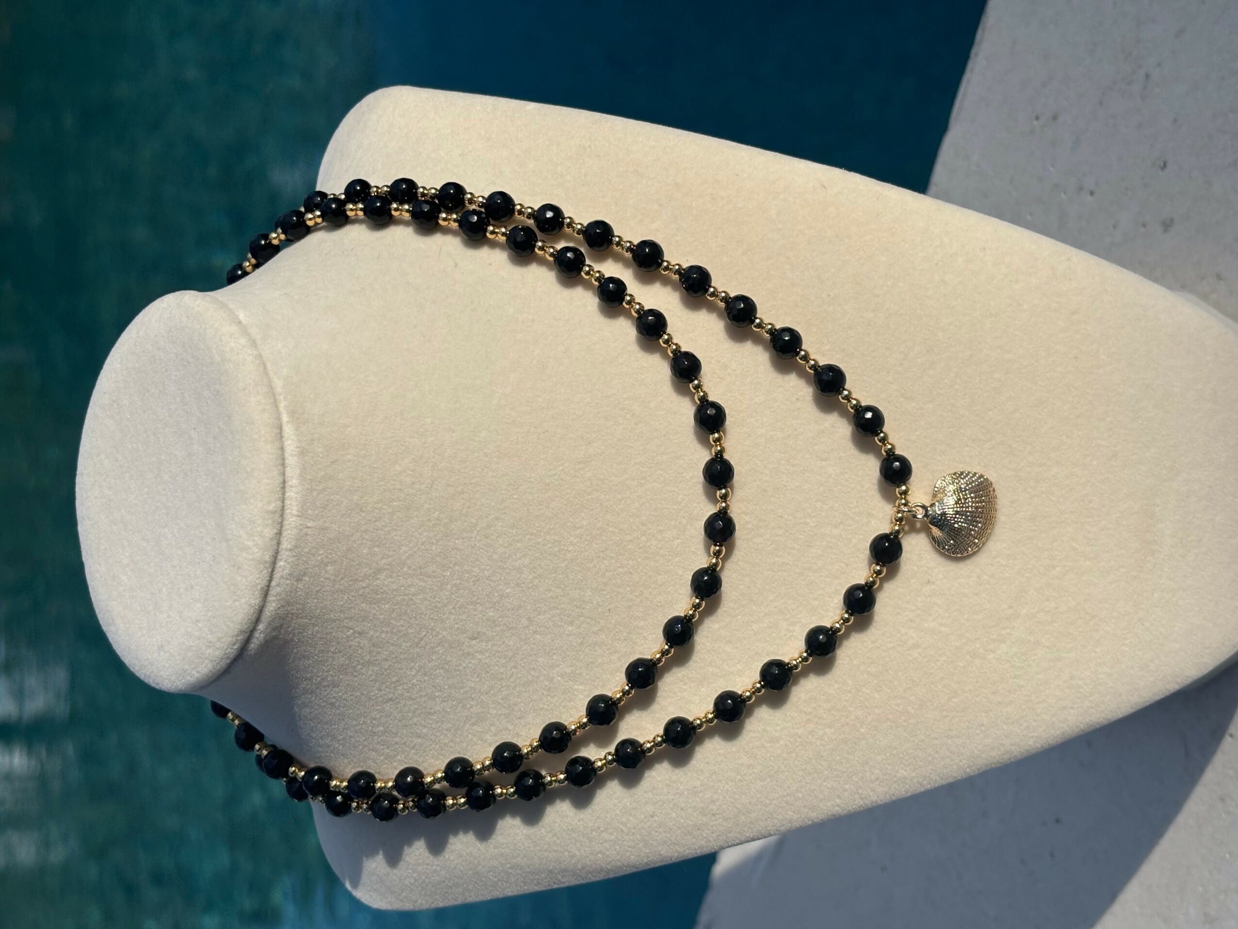 Two black beaded necklaces with a silver pendant displayed on a white jewelry stand.