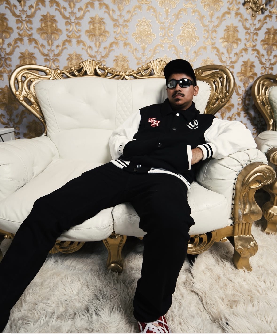 Person sitting on a luxurious white and gold sofa with a patterned gold and cream wallpaper background.
