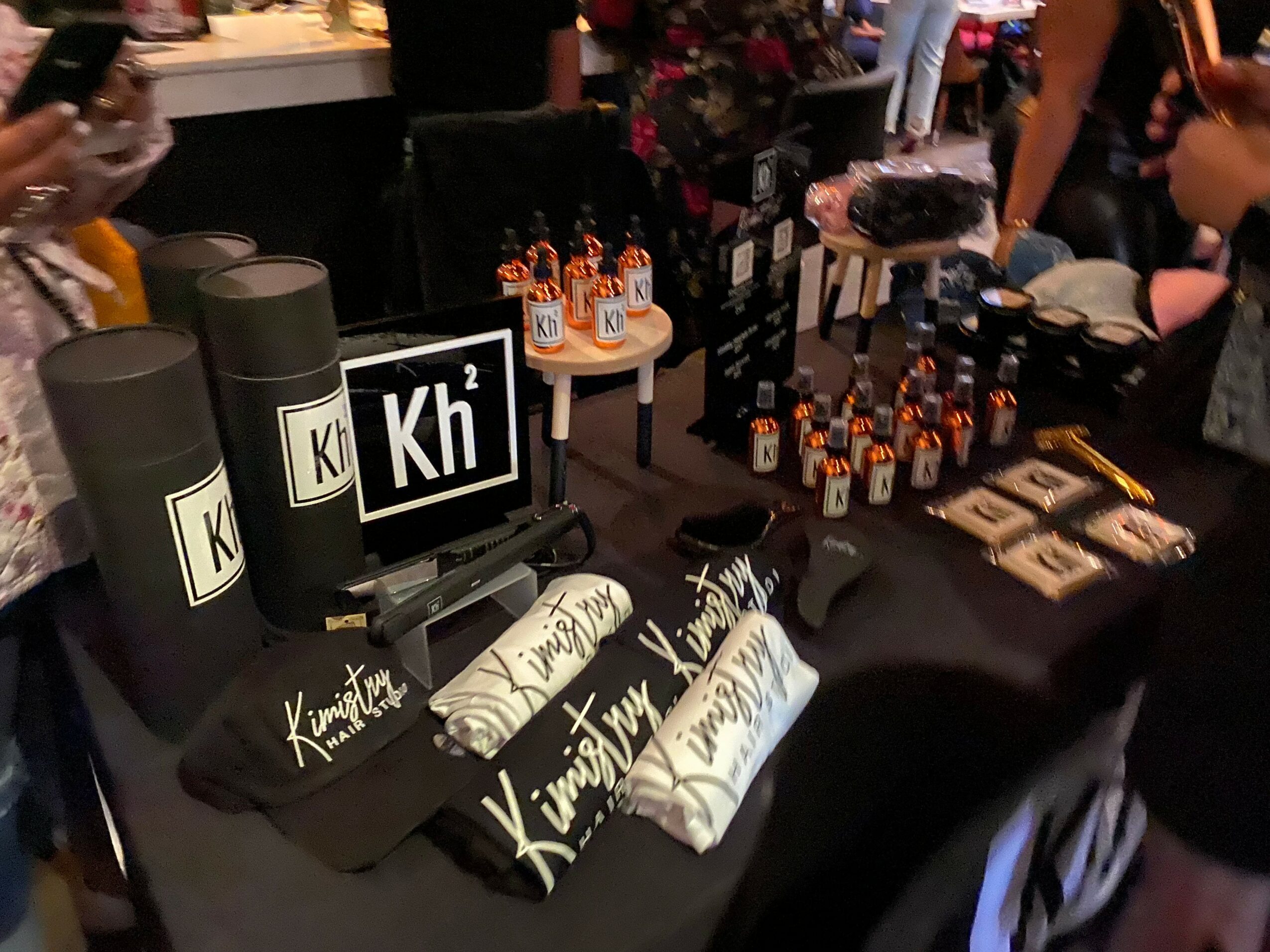 Table with black cylindrical containers, a sign with chemical symbol 'Kh', and various small bottles and items displayed.