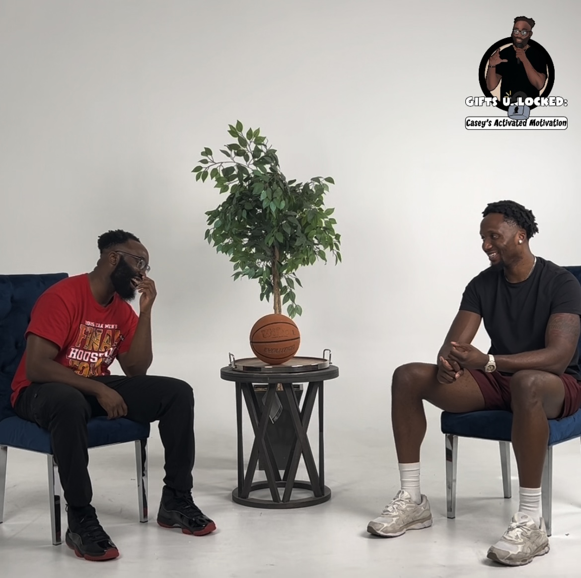 Two people sitting on chairs facing each other with a potted plant and basketball between them, against a plain white background.