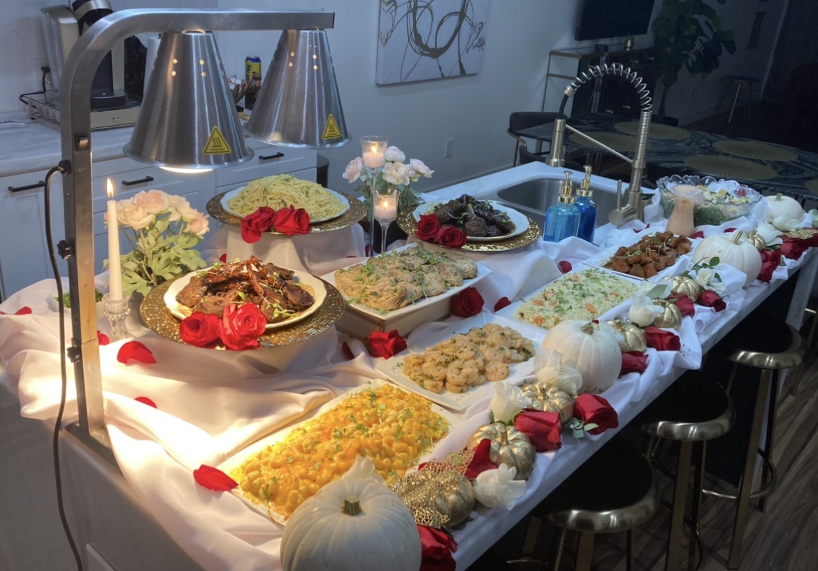 Buffet table with various dishes, flowers, and decorations, illuminated by overhead lights in a modern setting.