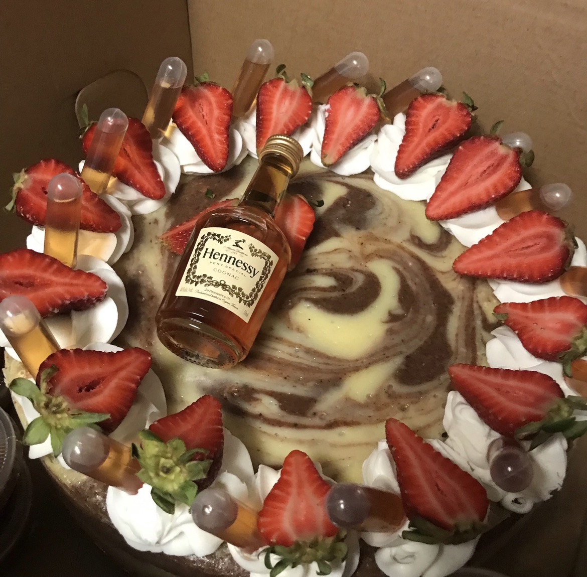 Chocolate and vanilla swirl cake with strawberries, grapes, whipped cream, and a small bottle of Hennessy in the center.