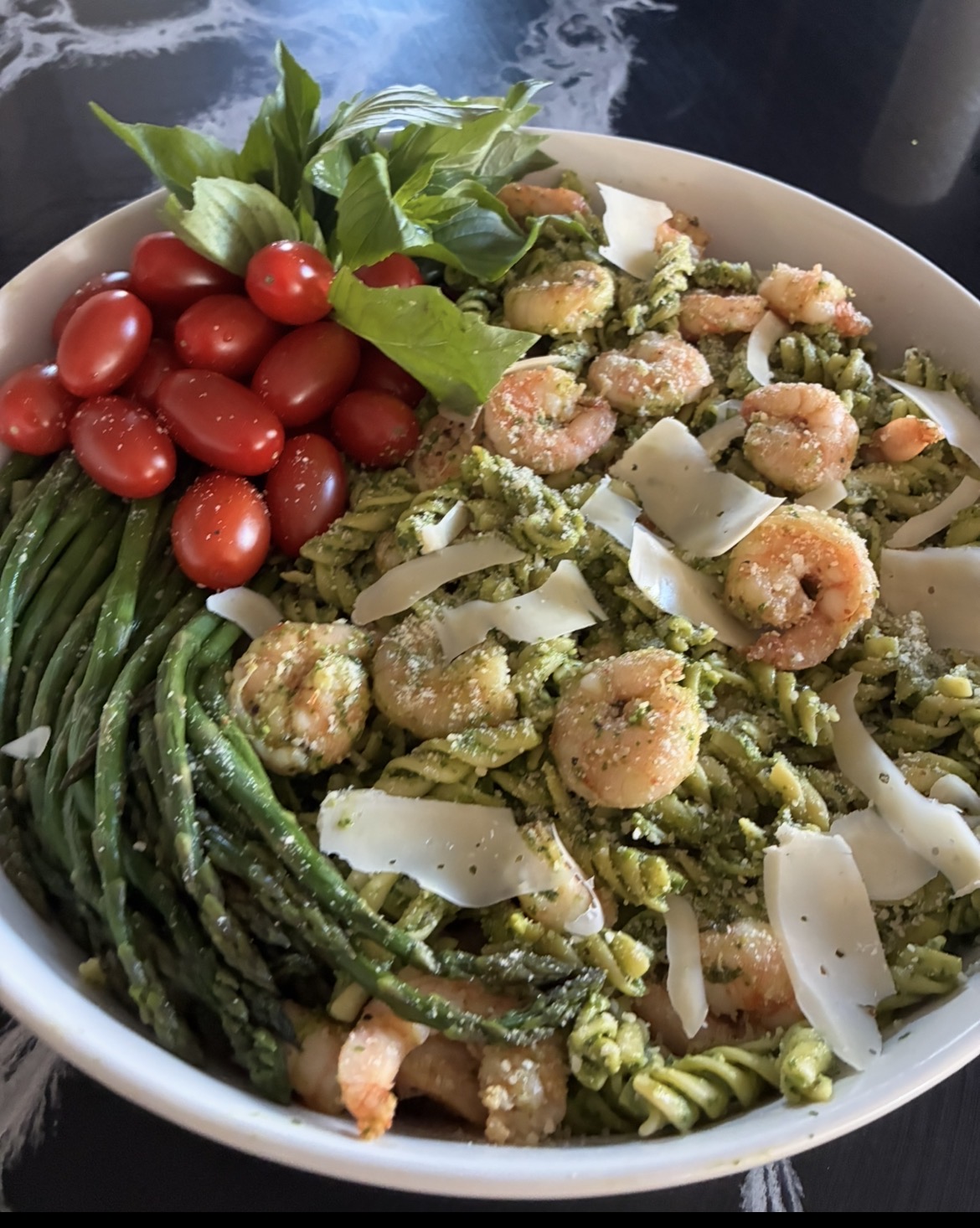 Bowl with cherry tomatoes, green beans, and a pasta salad with shrimp, broccoli, and cheese, garnished with basil leaves.
