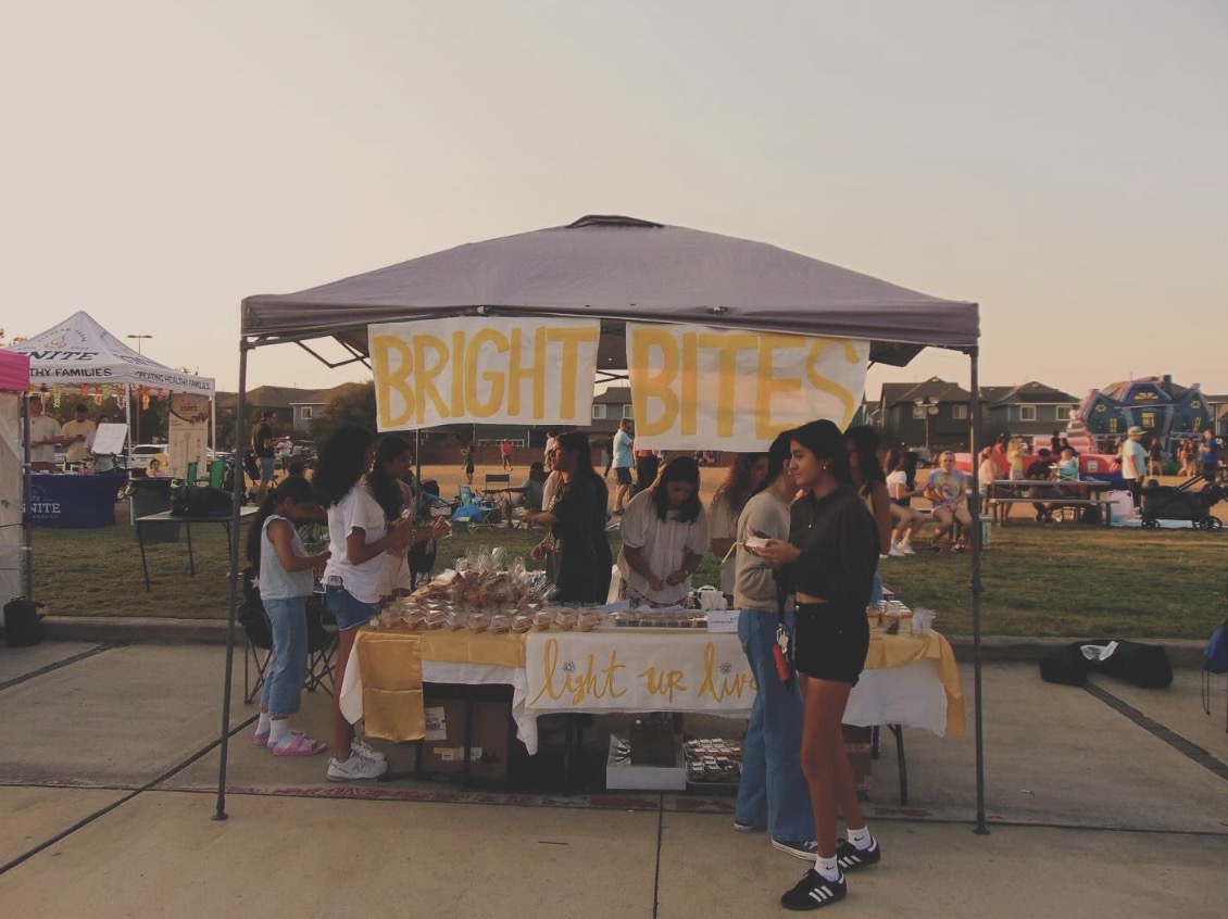 People gather around a booth with a yellow banner reading 'BRIGHT BITES' at an outdoor event.
