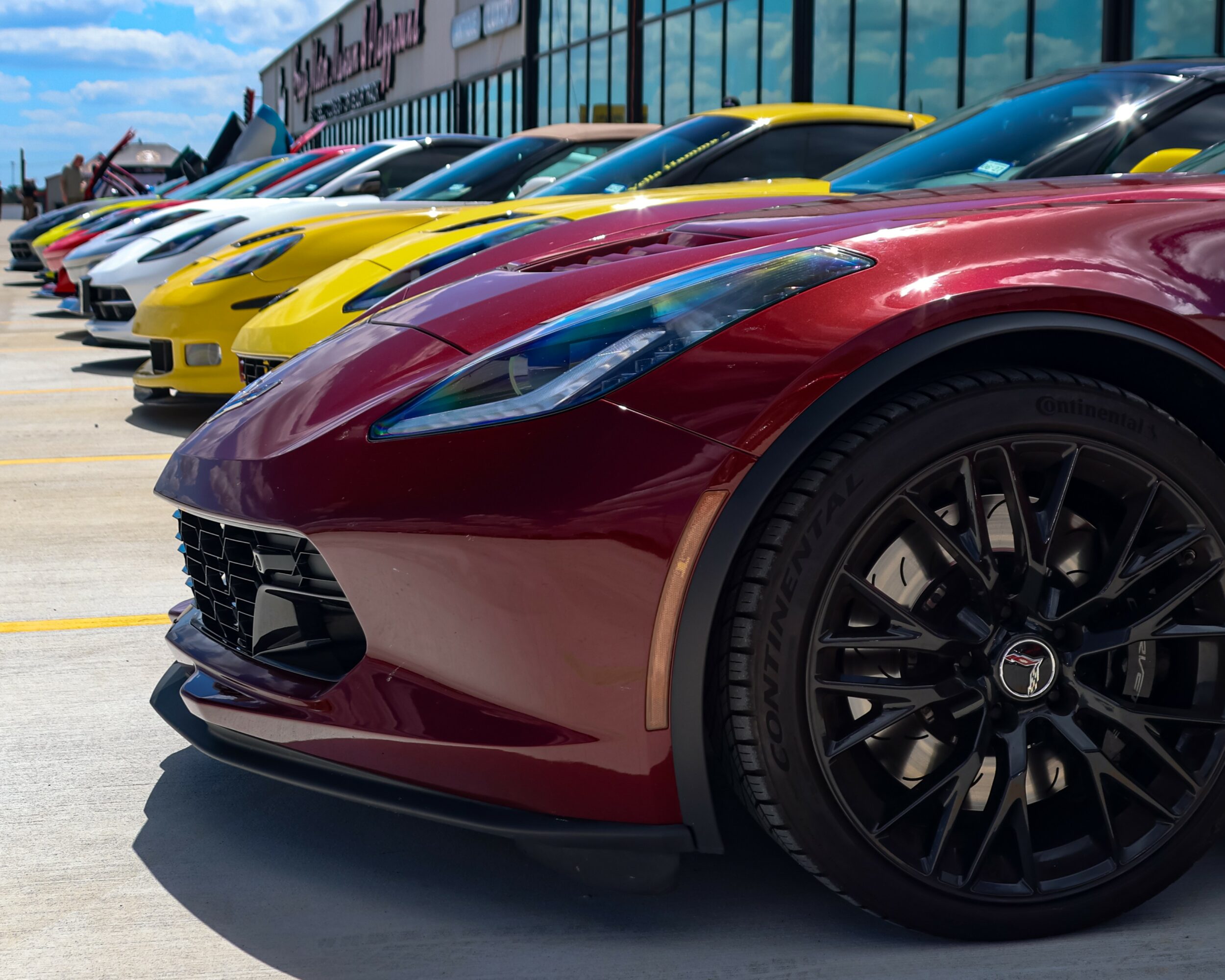 Lineup of colorful sports cars parked outside a building, with a red car in the foreground and others in yellow, white, and blue.