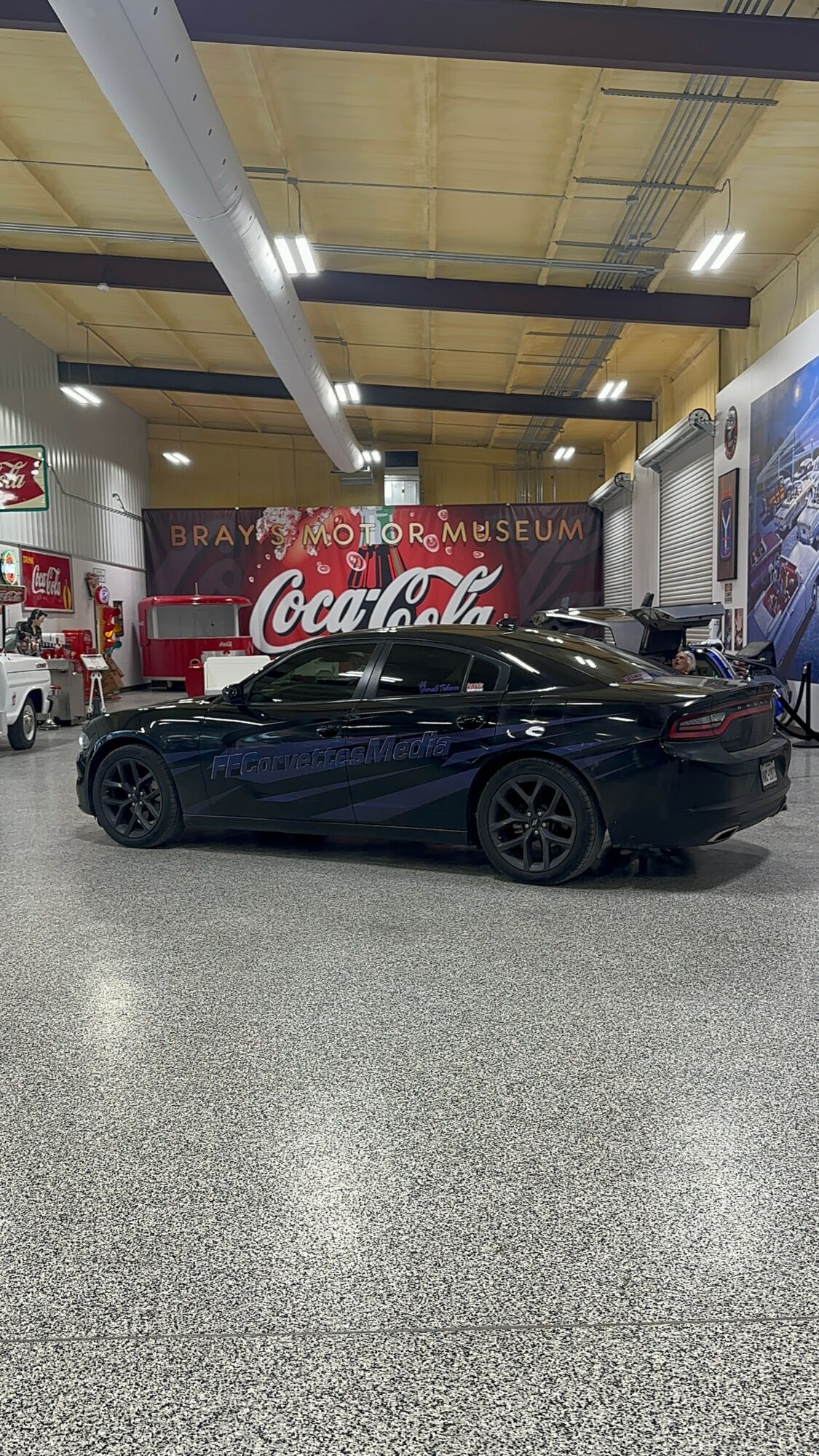 Black car parked indoors with Coca-Cola sign and museum signage in background.
