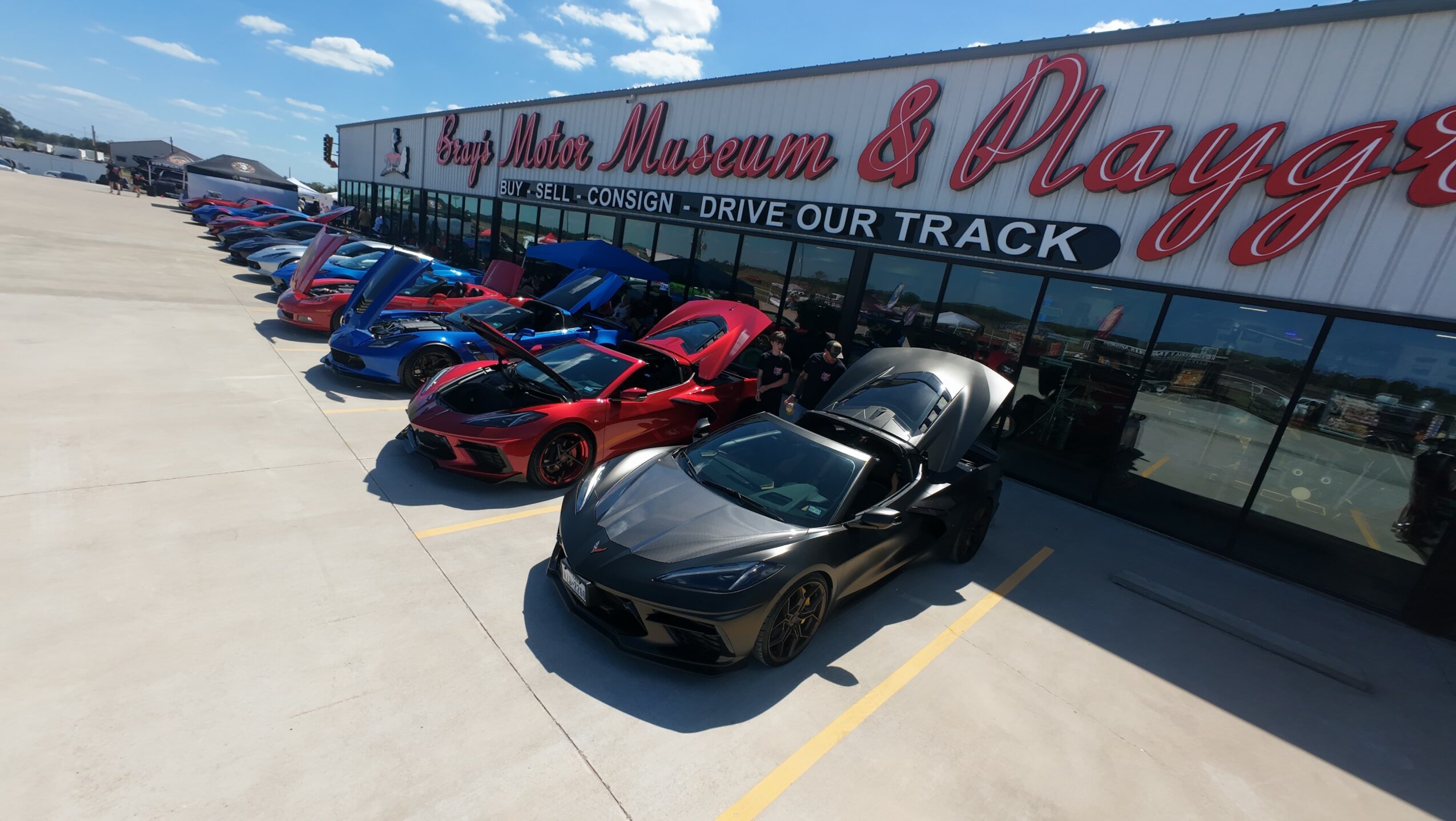 Multiple sports cars parked outside a museum with a sign reading 'Lamb Miss Museum & Playg'.