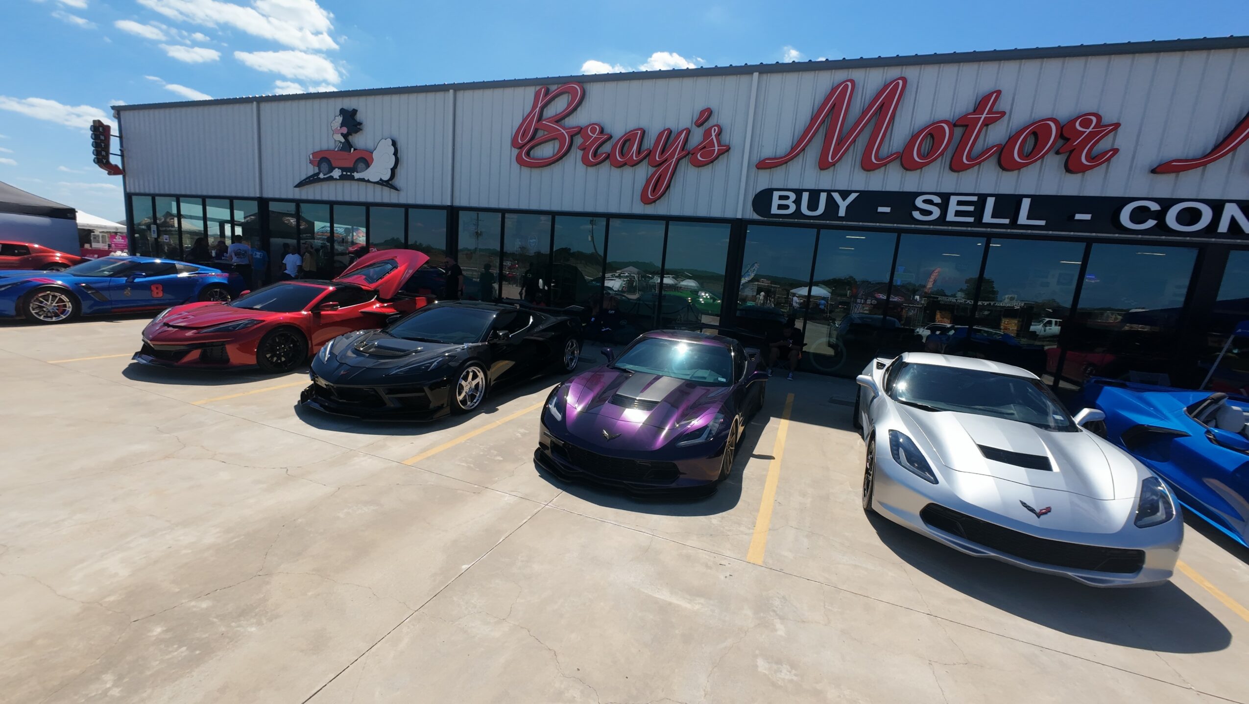 Five sports cars parked in front of a dealership with a sign reading 'Bray's Motor'.