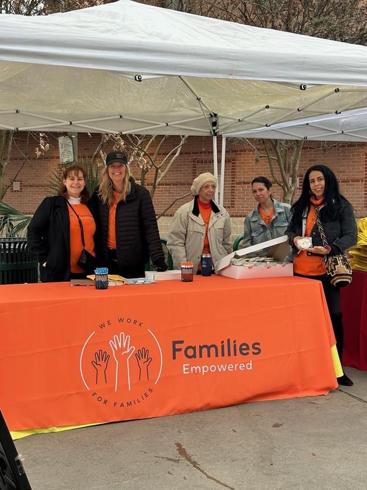 Five people stand behind a table with an orange banner reading 'Families Empowered' under a white canopy outdoors.