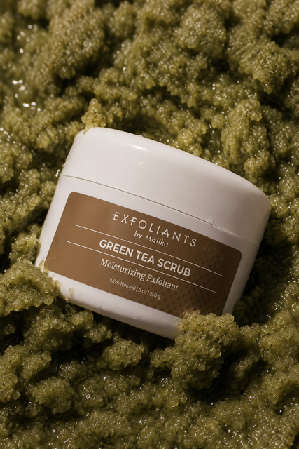 Container of exfoliant green tea scrub surrounded by green textured material, with a white lid and brown label.