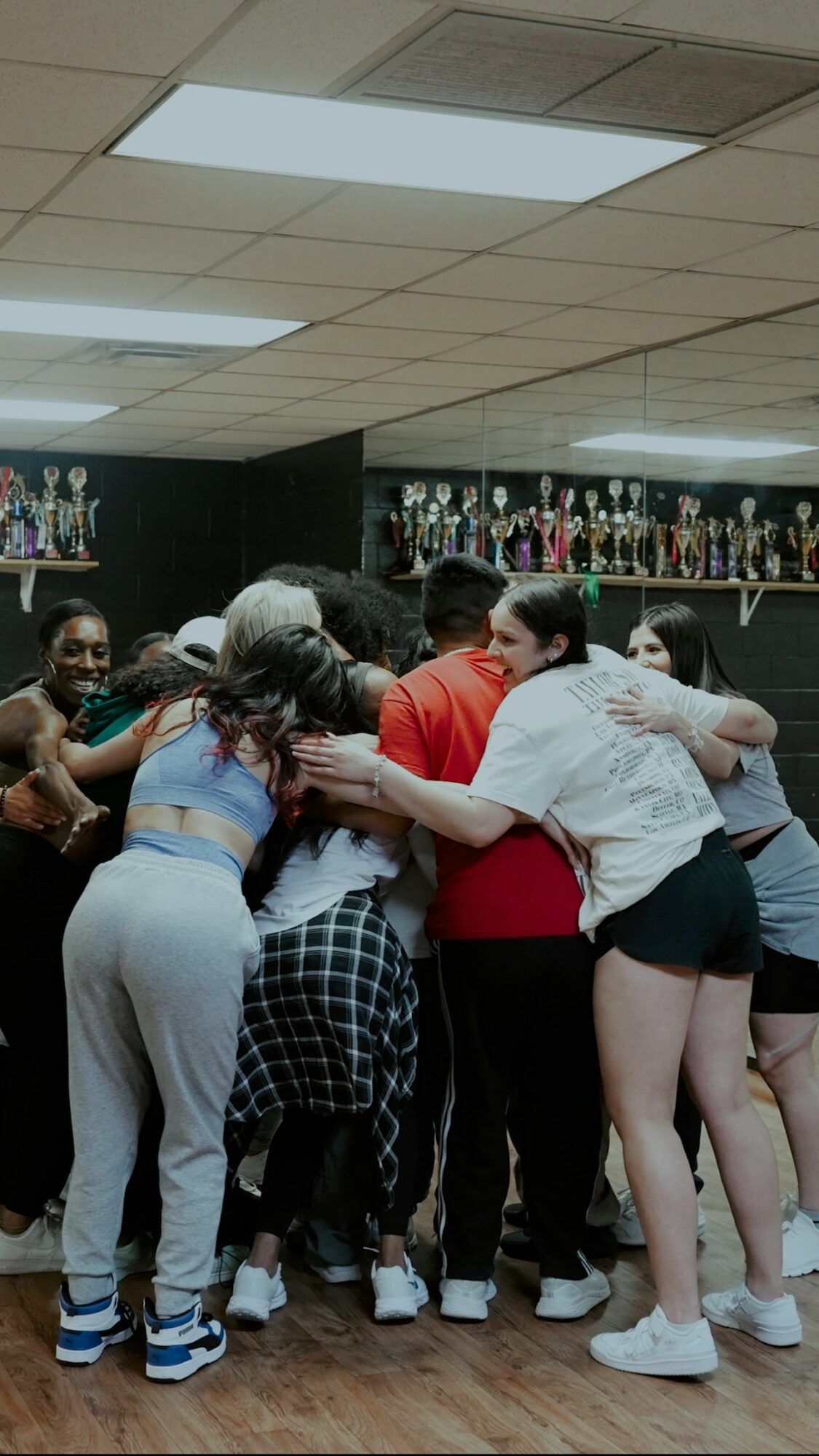 Group of people hugging in a room with trophies on shelves, celebrating together.