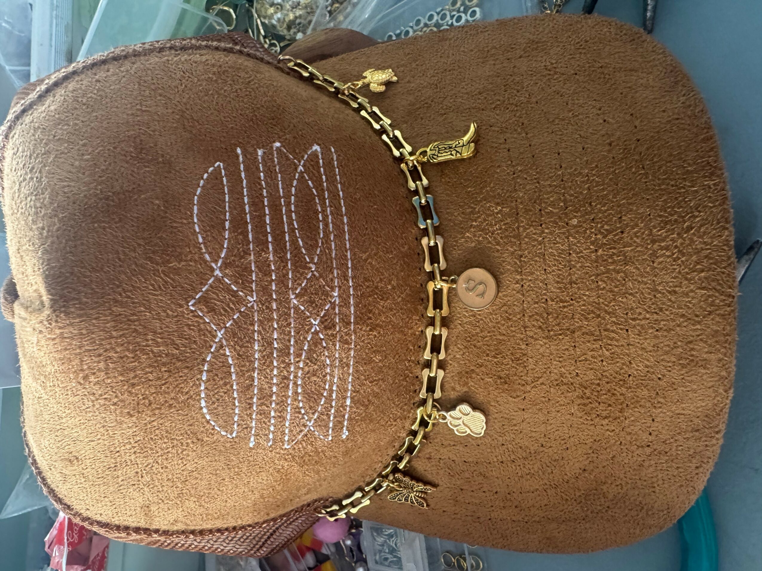 Brown plush bag with gold chain and zipper, embroidered design, and a small button, placed on a surface.