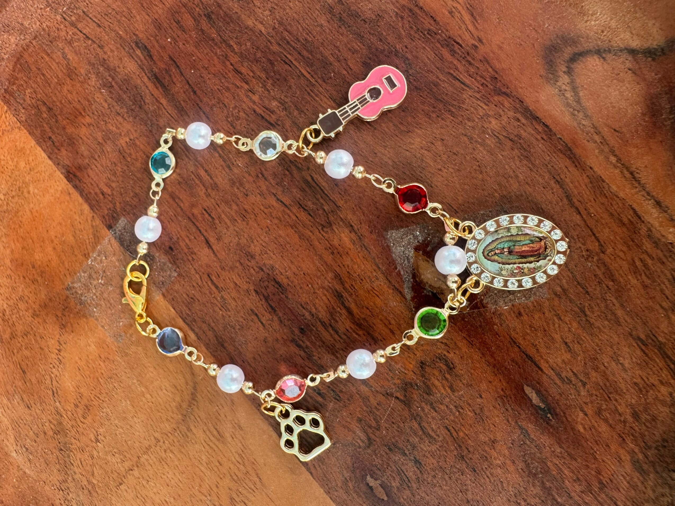 Colorful bracelet with charms and beads on wooden surface, featuring a pink guitar, a silver oval, and a paw print charm.