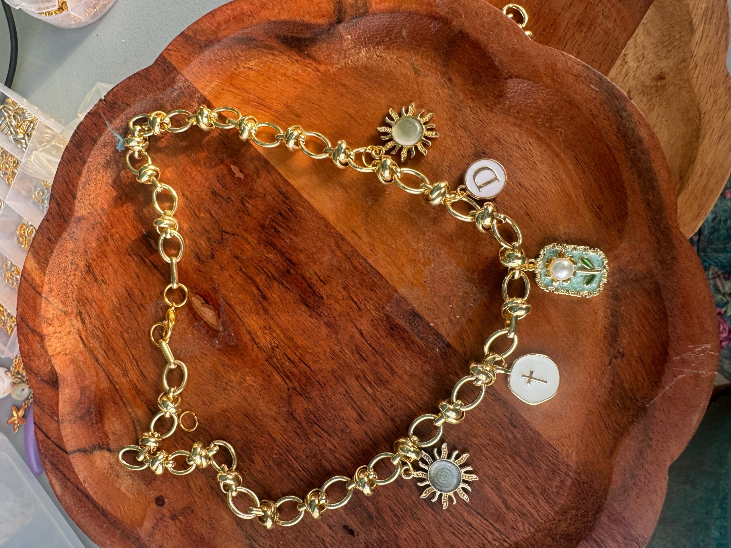 Gold chain necklace with sun and flower charms on a wooden surface.