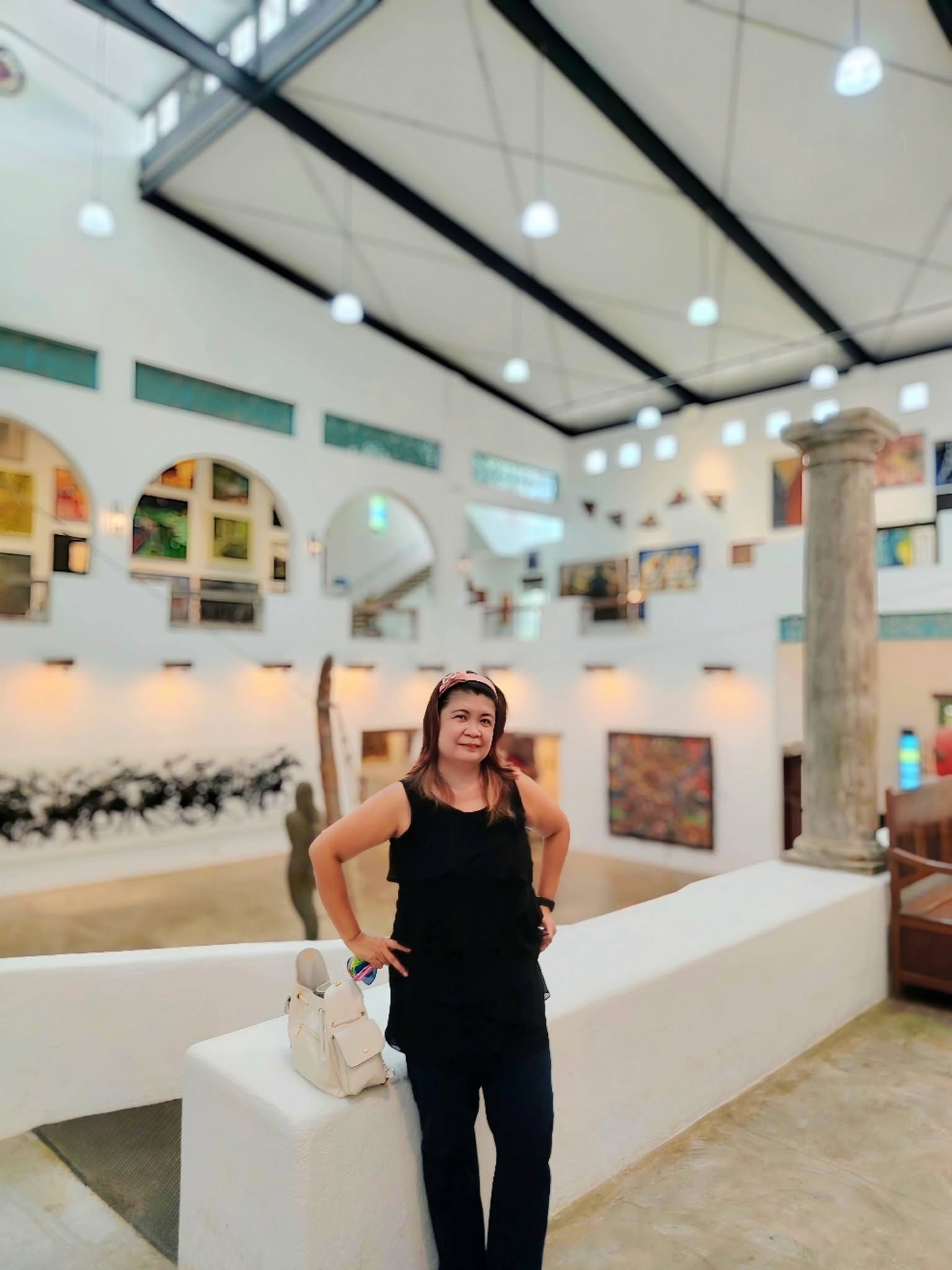 Woman standing indoors with artwork and architectural features in the background.