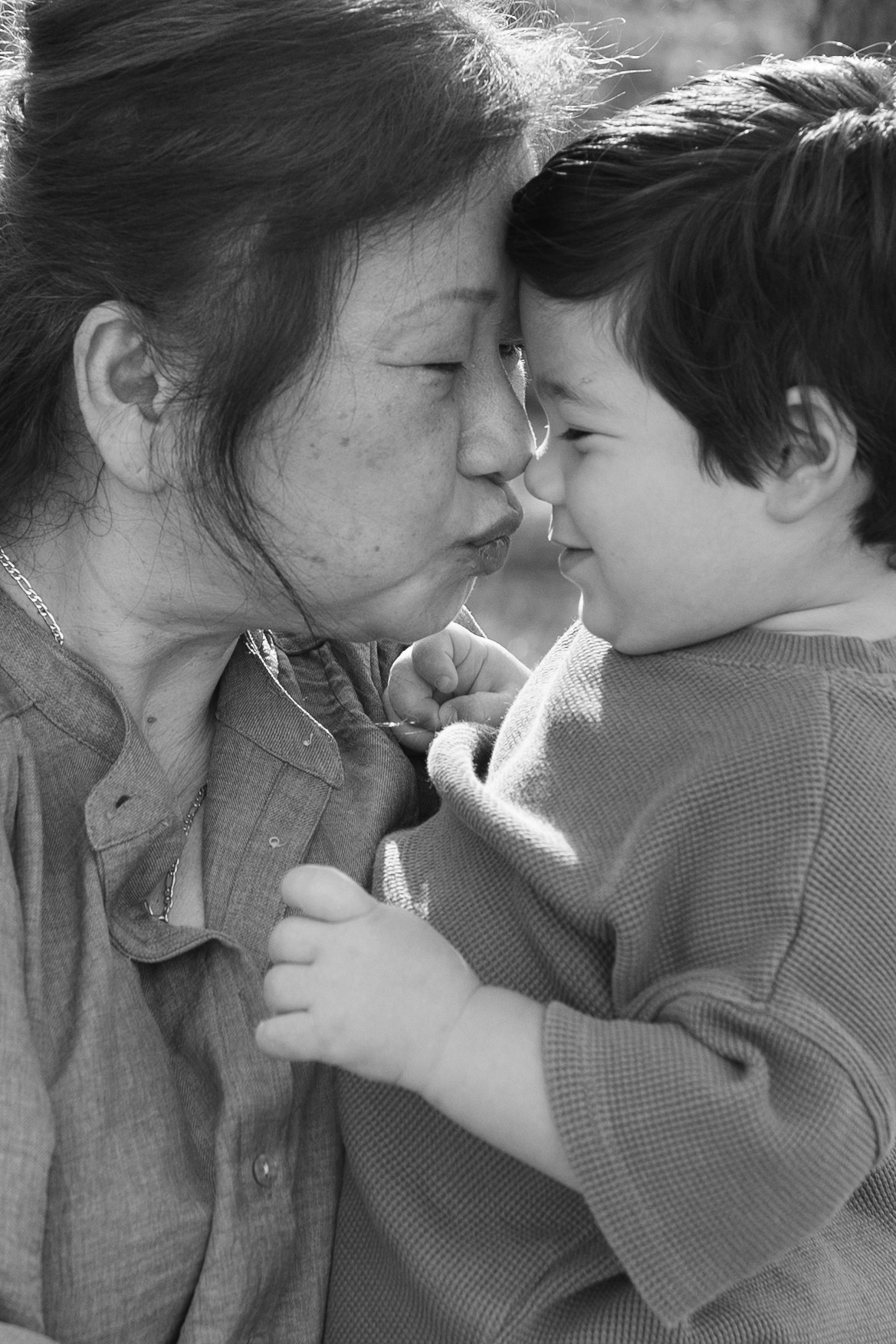 An elderly woman and a young child touch foreheads, eyes closed, sharing a tender moment.