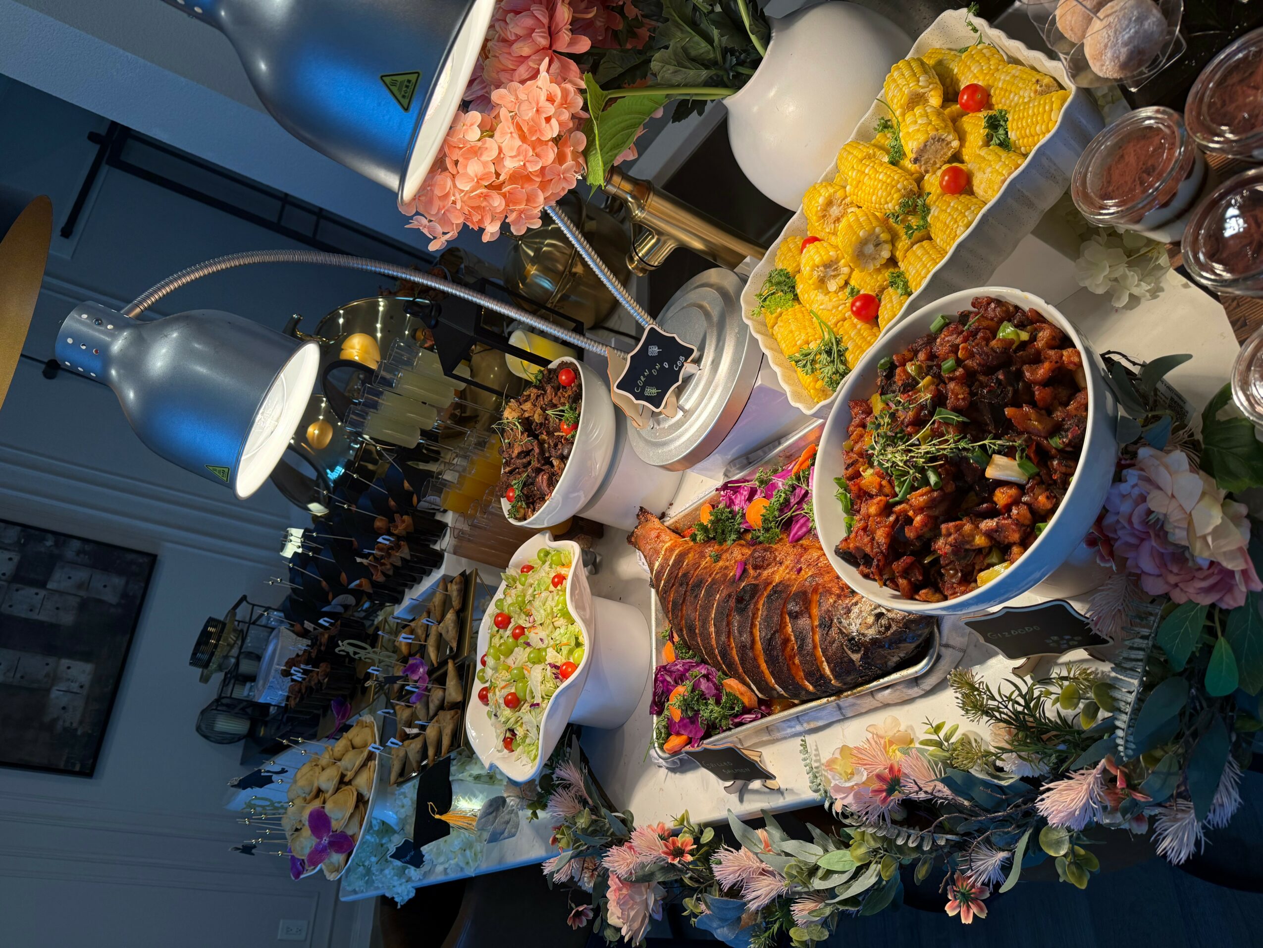 Table with various colorful desserts and flowers, viewed from the side, with a floral tablecloth.