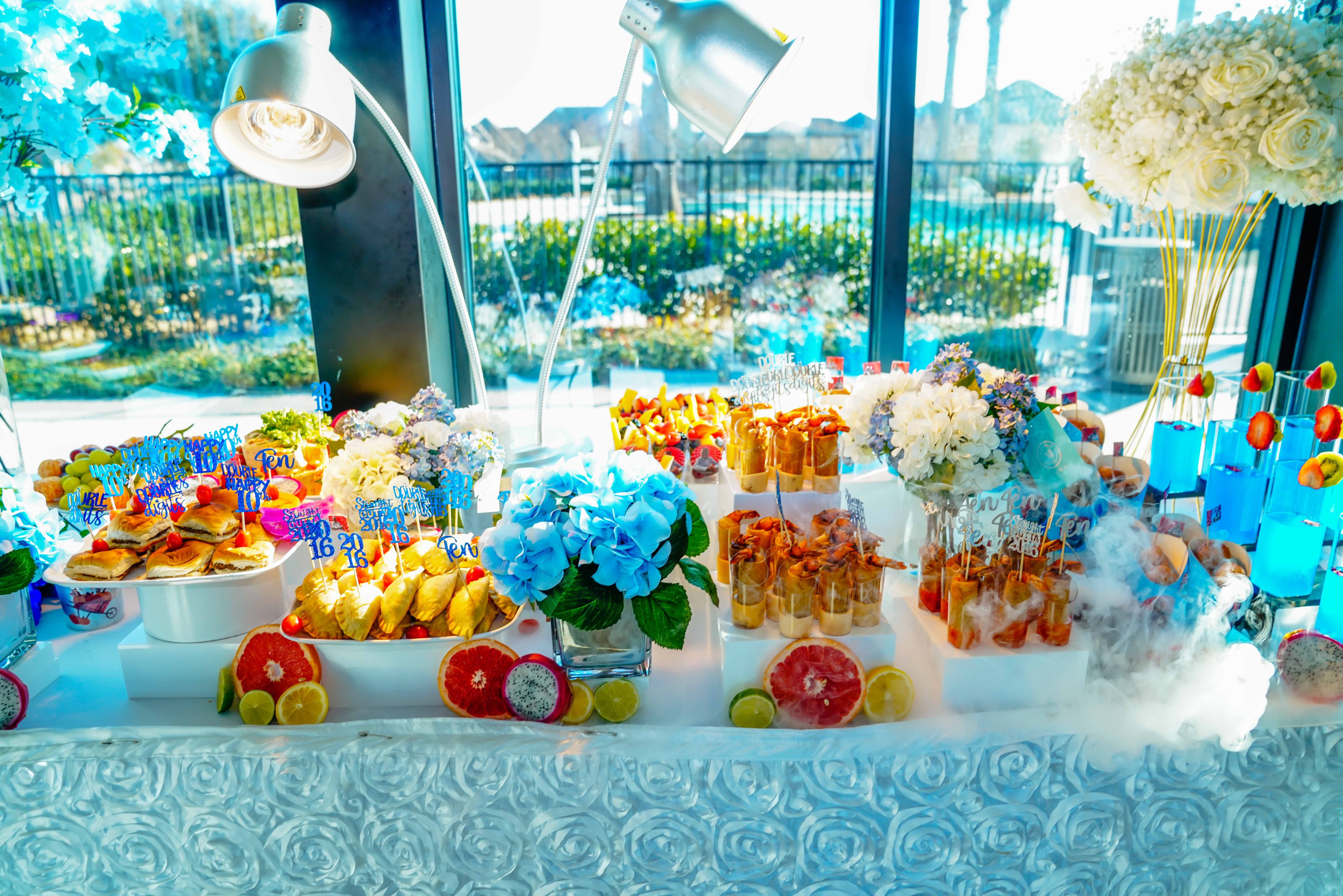Table with colorful desserts, flowers, and decorations near a window with outdoor view