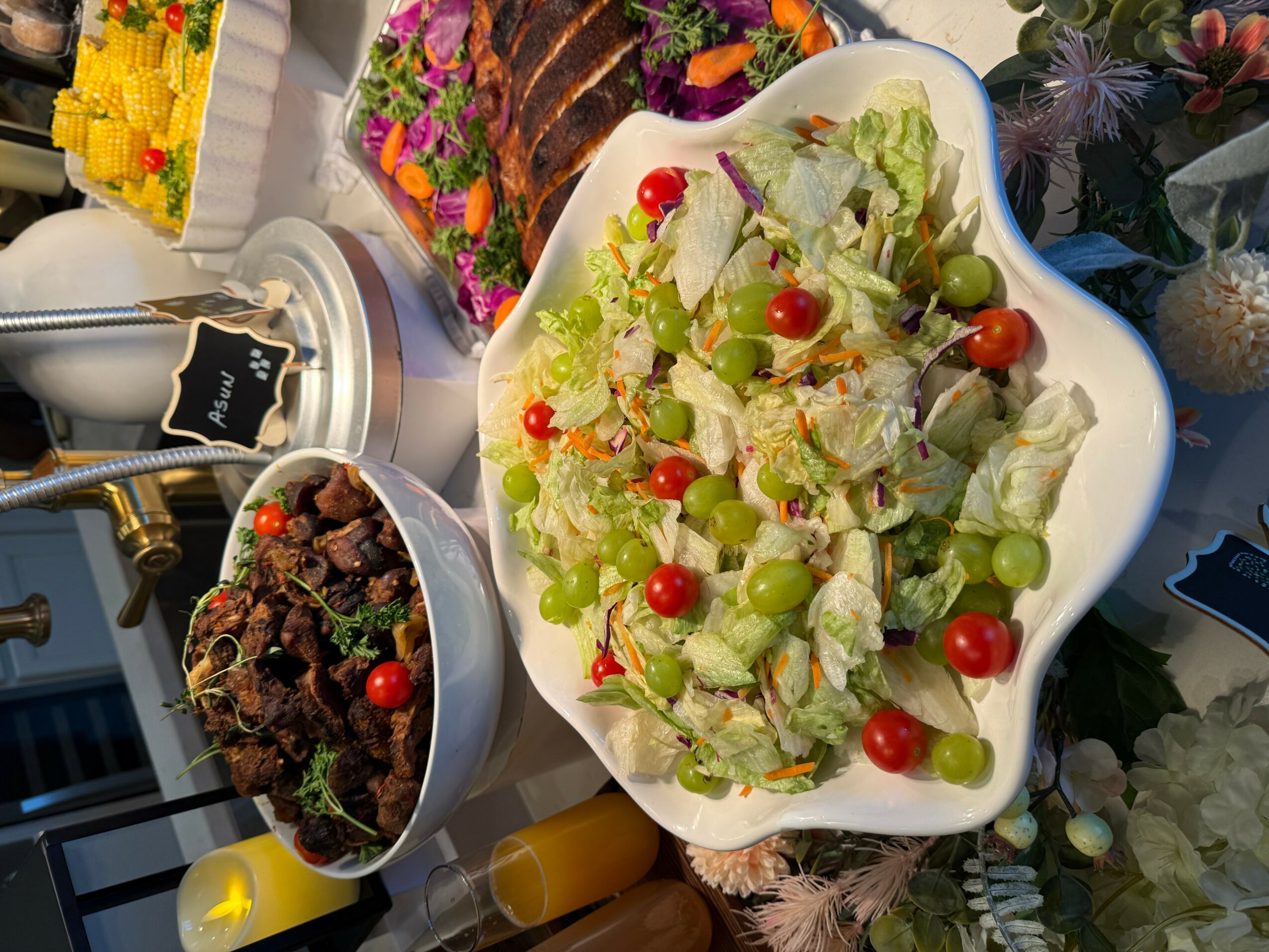 Fresh salad with lettuce, cherry tomatoes, and green grapes in a white bowl, with other dishes and decorations nearby.