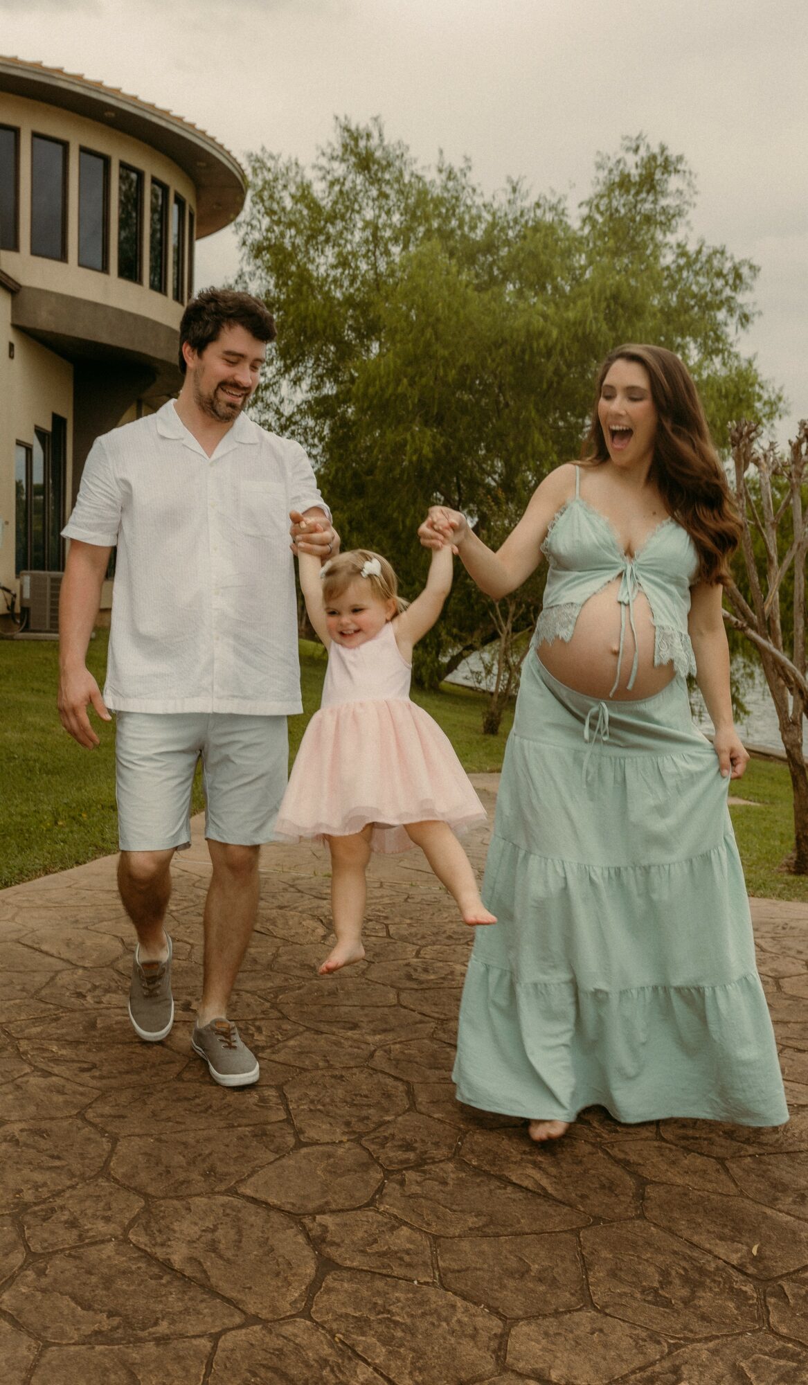 Family of three walking outdoors, holding hands, with a building and trees in the background.