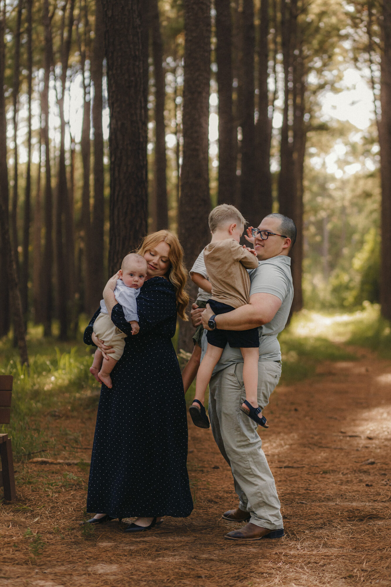 Family of four standing on a forest path, trees in the background, sunlight filtering through the trees.