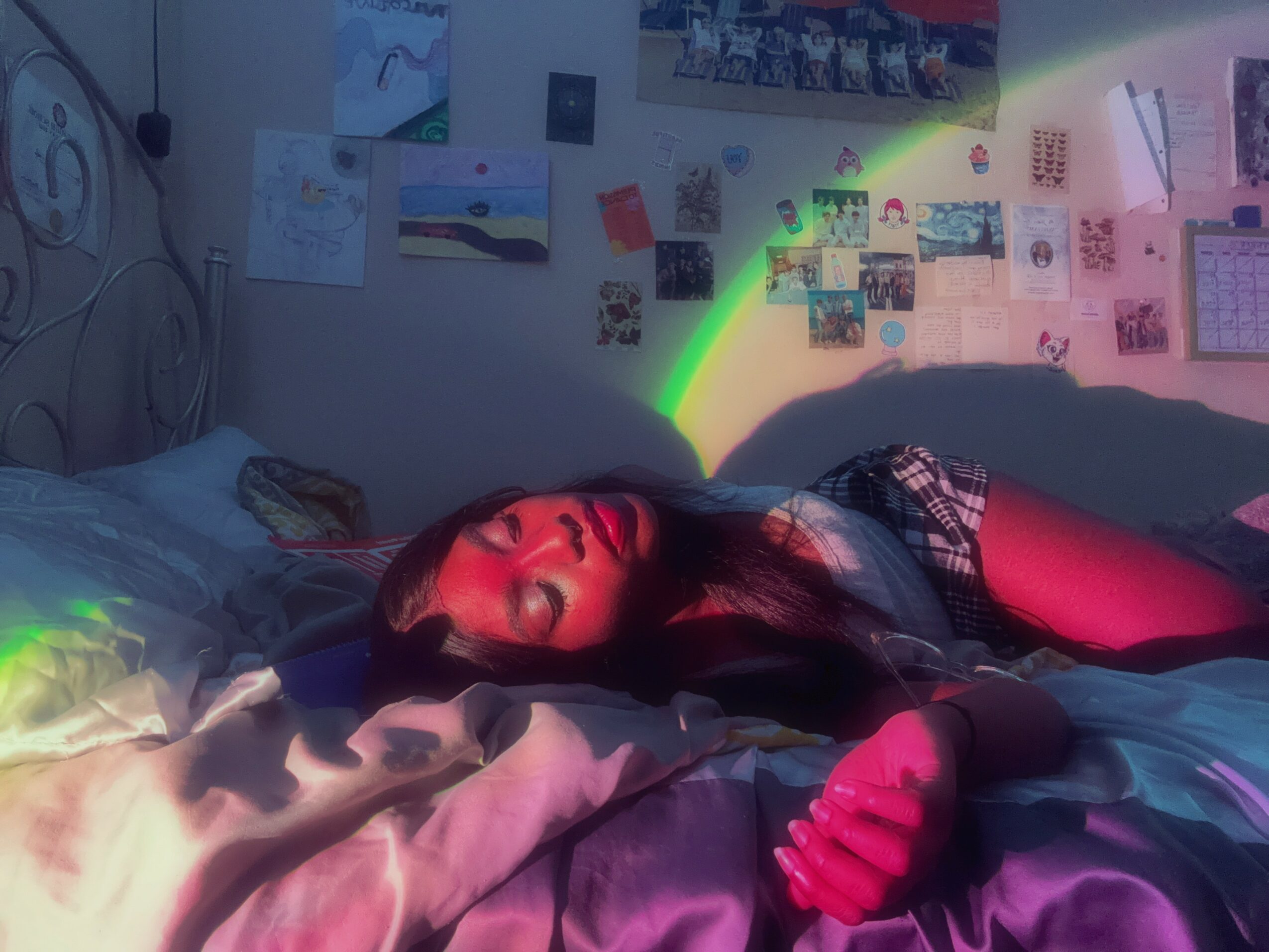 Person lying on bed with eyes closed, colorful lights and wall decorations in background.