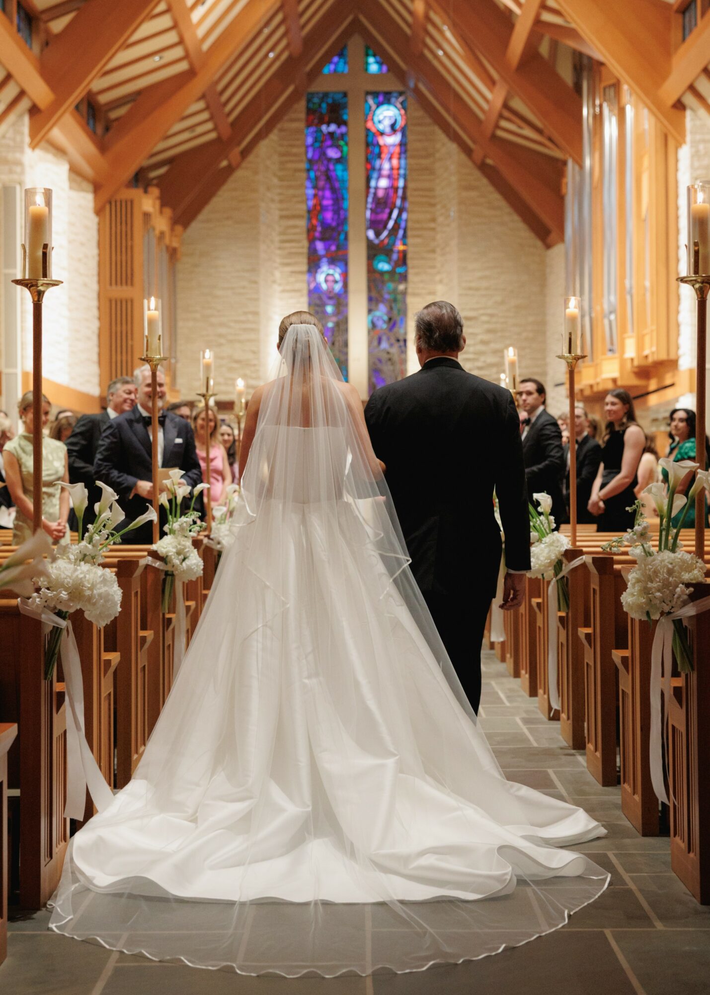 Bride and groom walking down the aisle in a church with stained glass window, wooden interior, and guests on both sides.