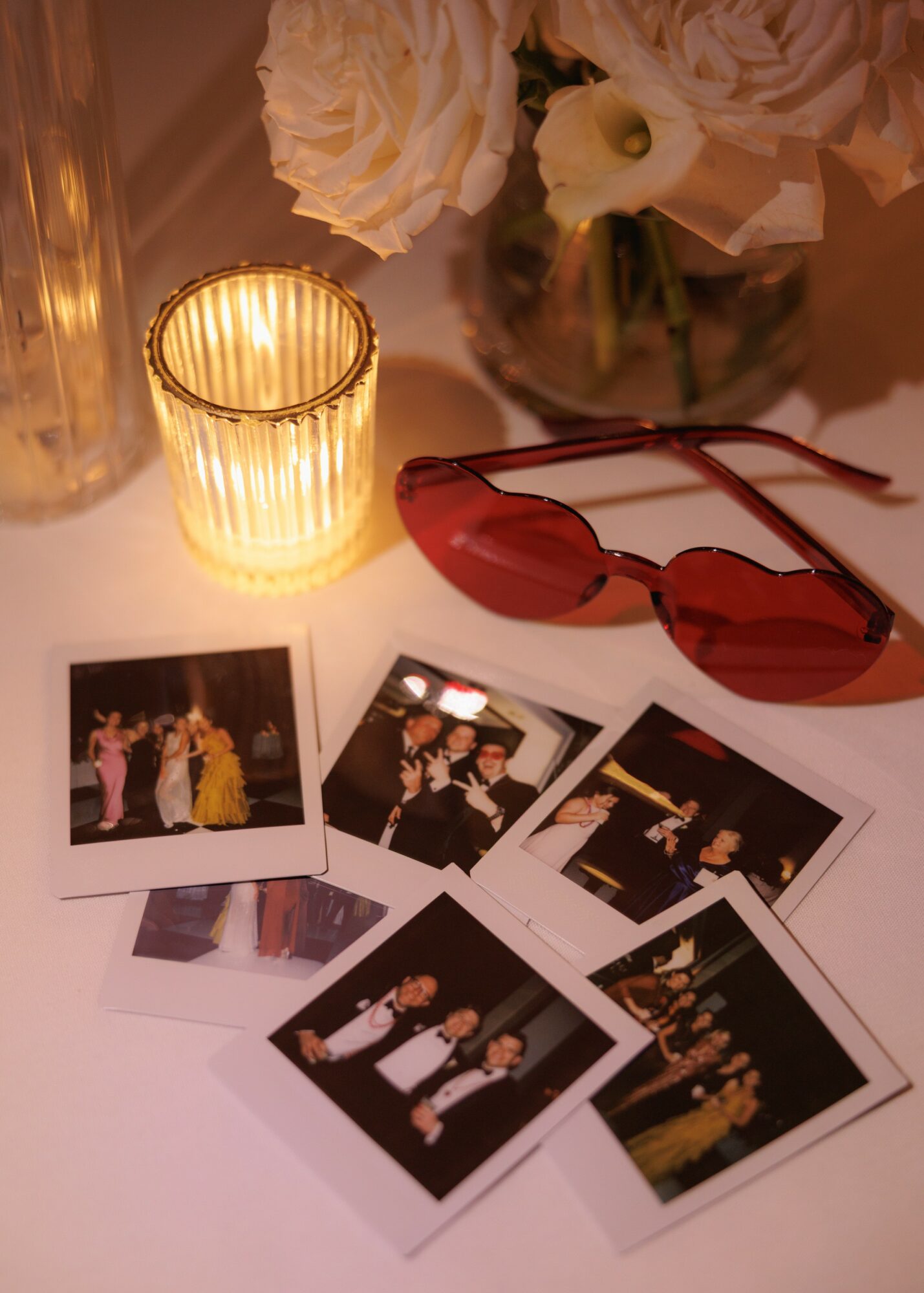 Photographs, red sunglasses, a candle, and flowers on a table, with soft lighting creating a warm atmosphere.