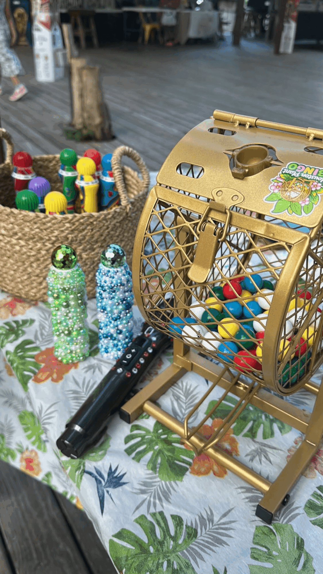 Table with colorful game pieces, a basket of wooden pegs, and a gold game device, outdoors setting.