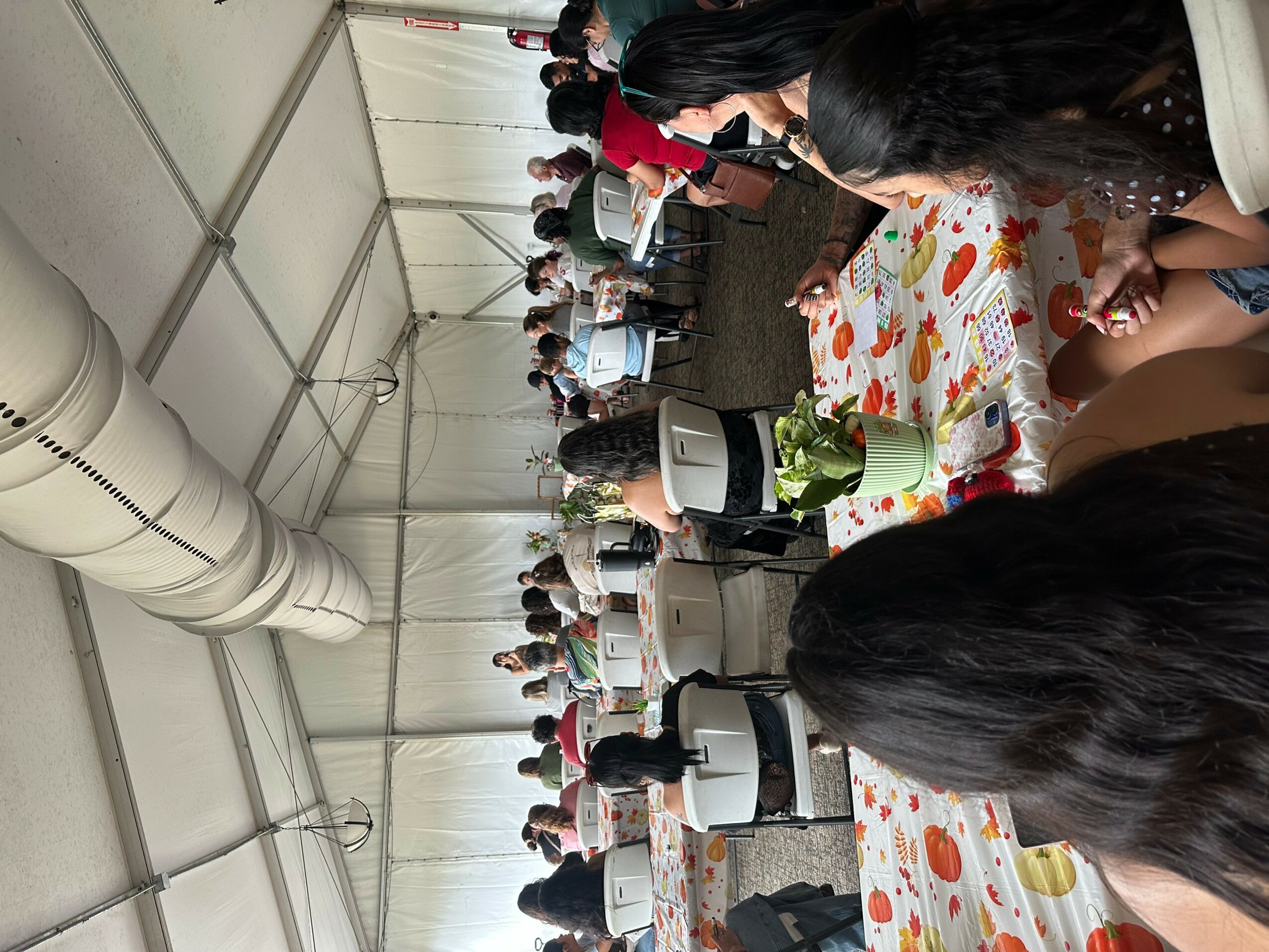 People gathered inside a large tent, sitting at tables with colorful tablecloths, engaged in activities or conversations.