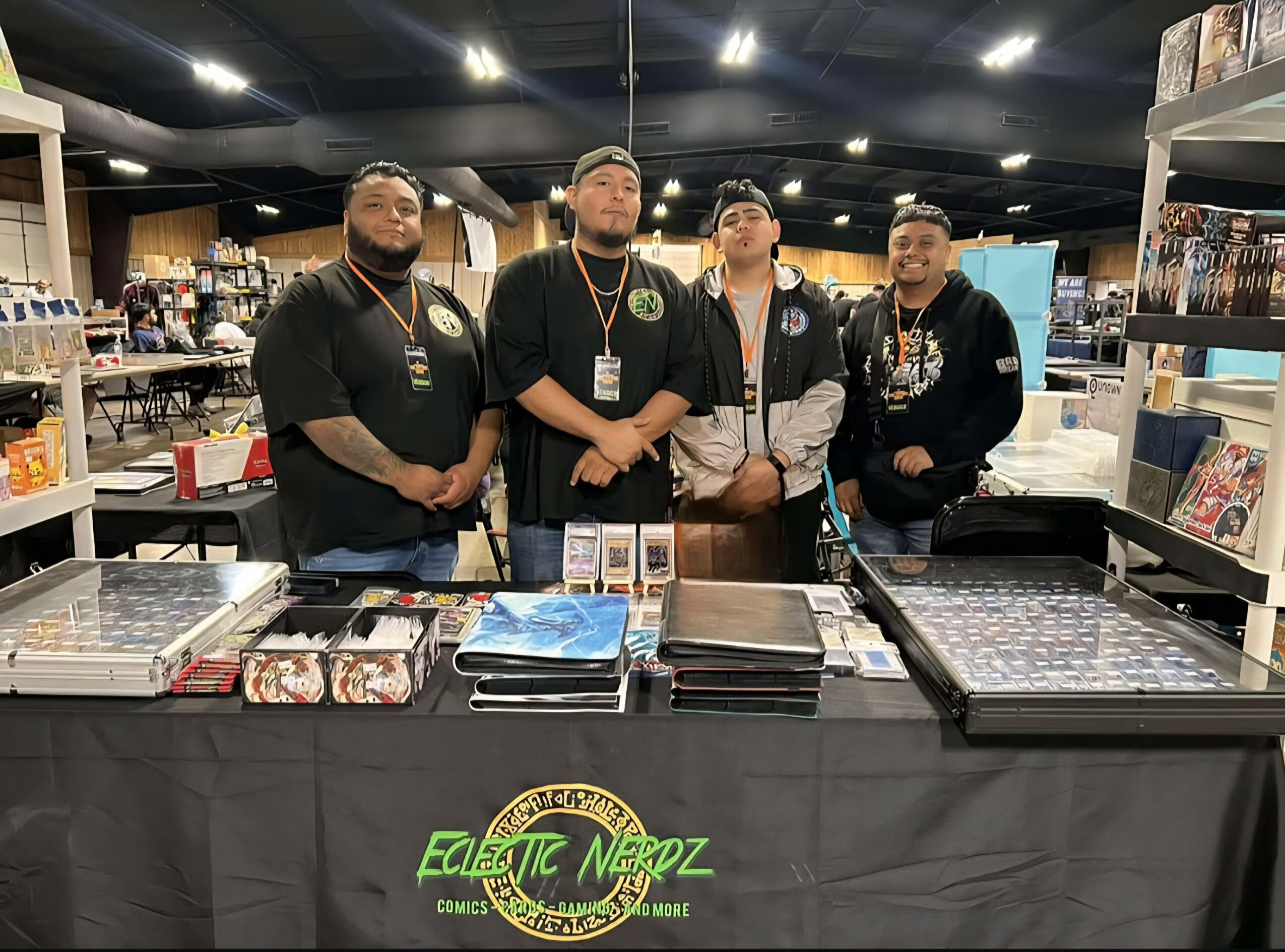 Four people stand behind a table at a convention booth with shelves of comics and merchandise in the background.