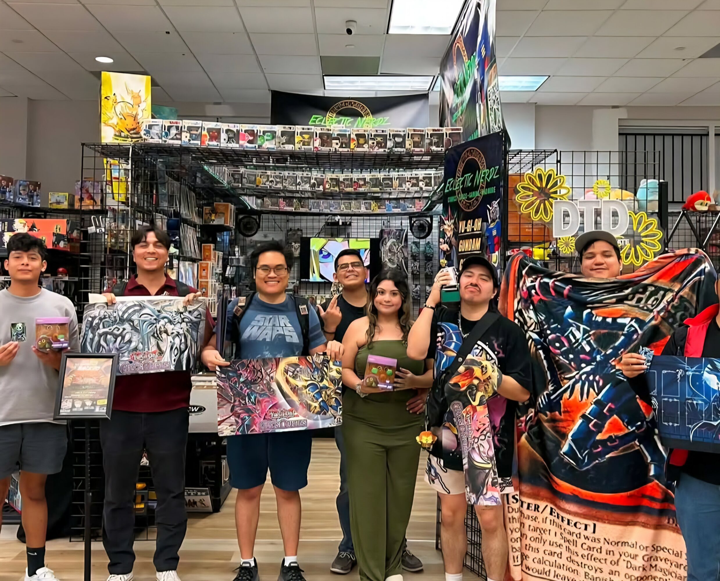 Six people stand in a store aisle holding colorful merchandise, with shelves and signs in the background.