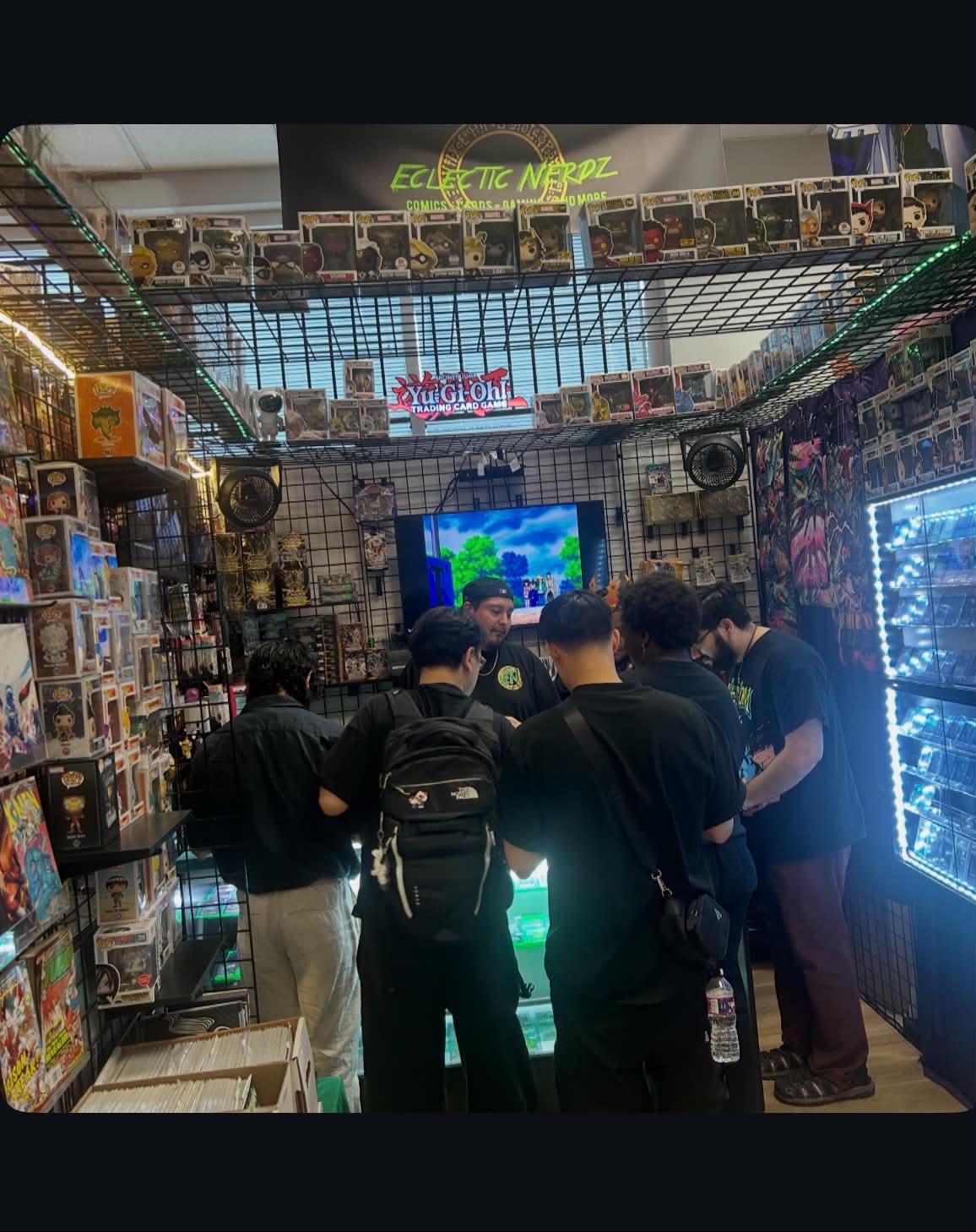 Group of people inside a store looking at a screen, surrounded by shelves of products and colorful lights.