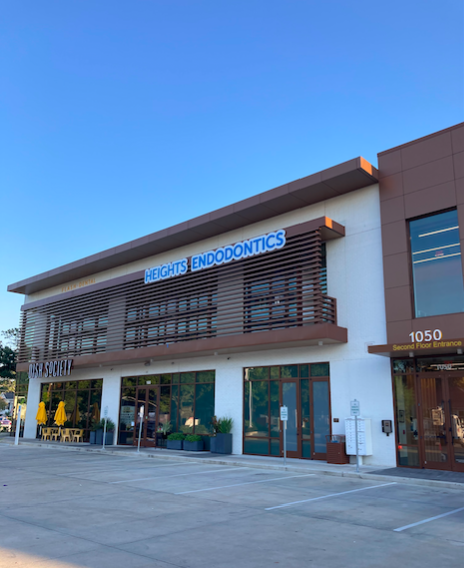 Modern building with a sign for endodontics, large windows, and a parking lot in front, under a clear blue sky.