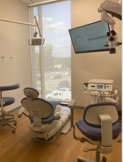 Dental clinic room with chair, monitor, and equipment near window, sunlight outside, clean and organized space.