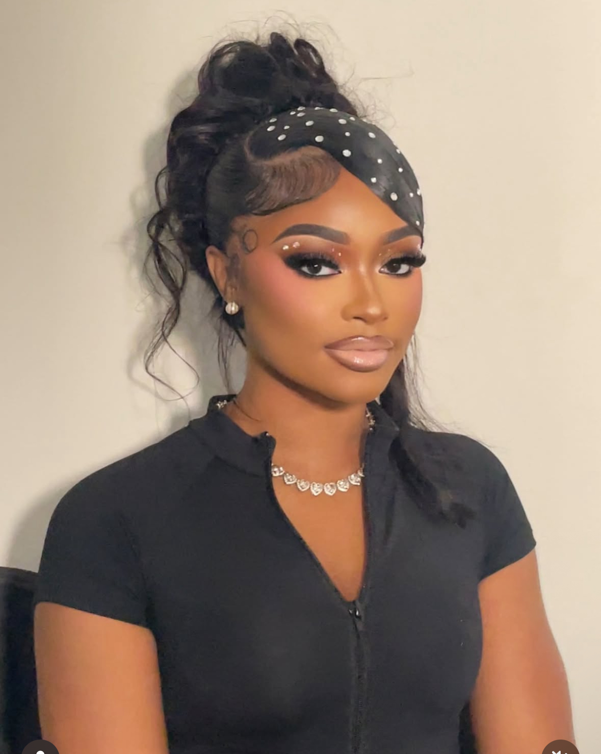 Young woman with styled hair, makeup, and a polka dot headband, wearing a black top and jewelry, looking at the camera.