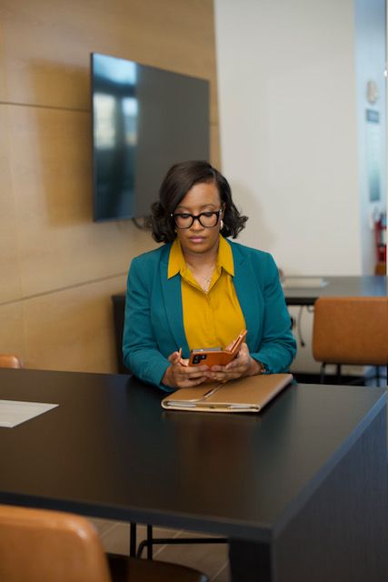 Woman in glasses and colorful blazer working at a desk with a laptop, in a modern office setting.