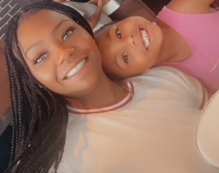 Two smiling females lying close together, one with braided hair and the other with short hair, in a relaxed setting.