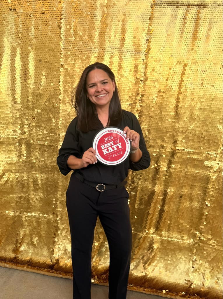 Woman smiling holding a red and white sign in front of a gold backdrop.