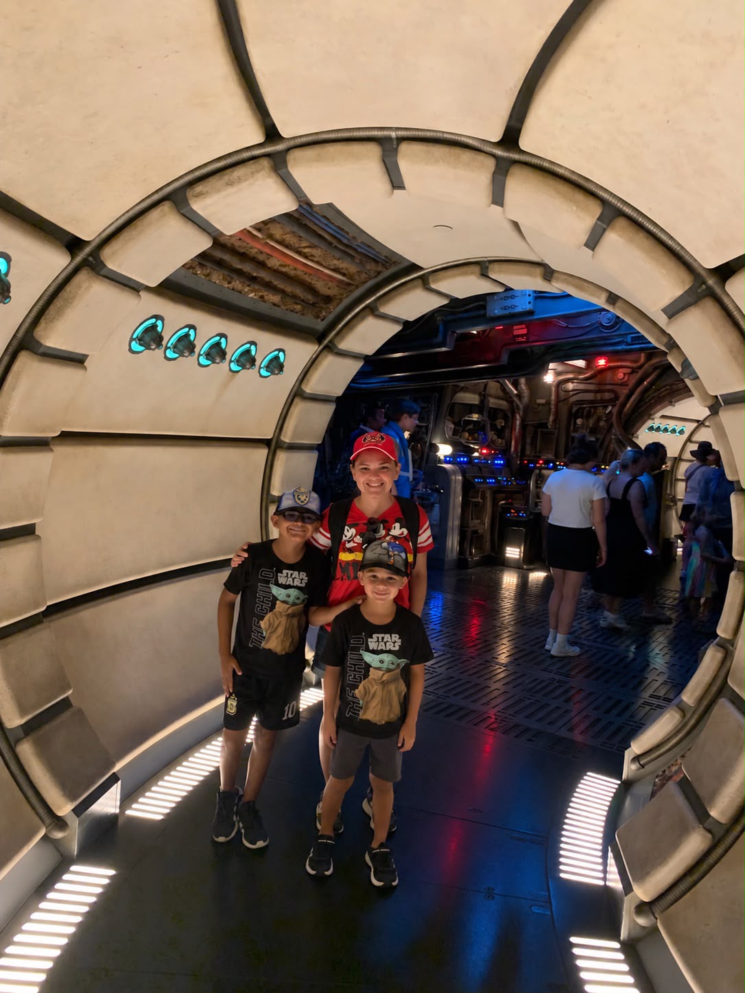 Three children and an adult pose inside a circular metallic structure with a futuristic design, in a busy indoor setting.