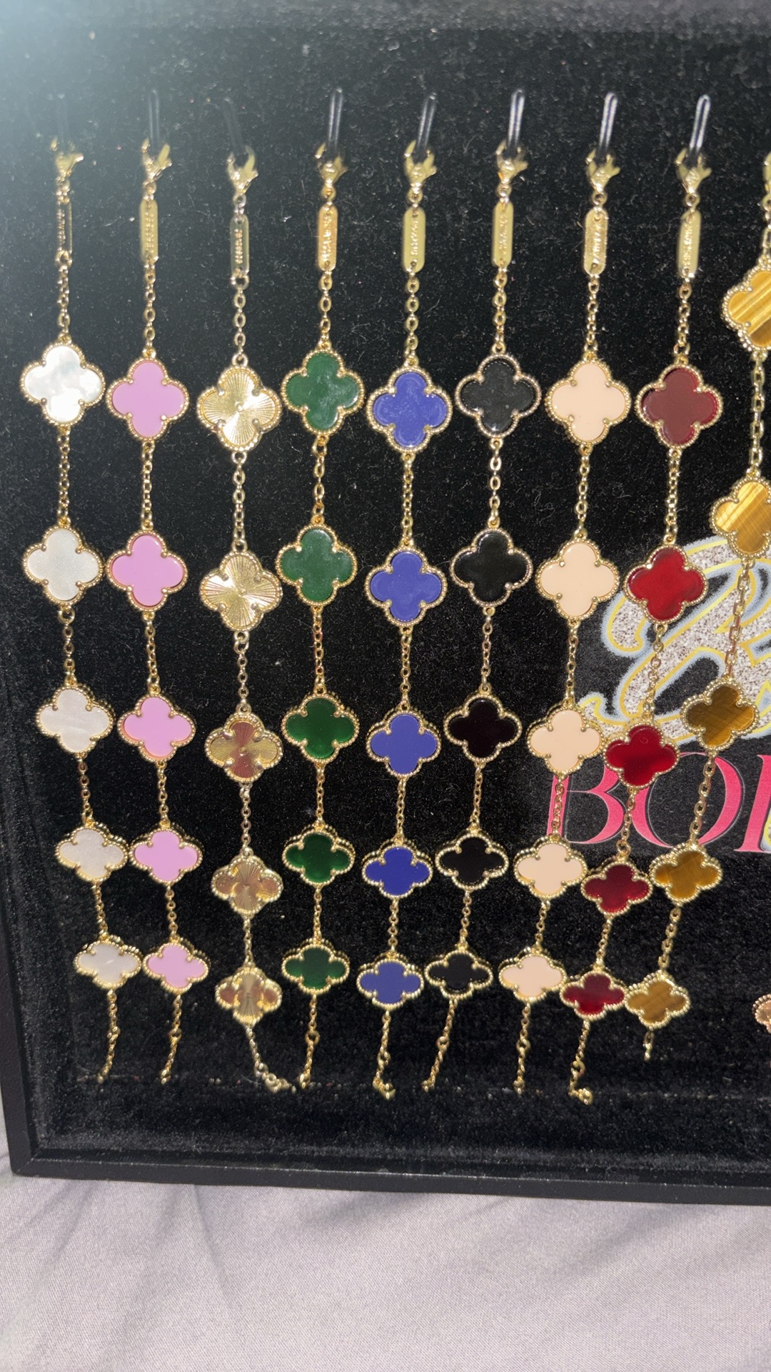 Display of colorful chain necklaces with floral and geometric patterns, arranged vertically in a case.