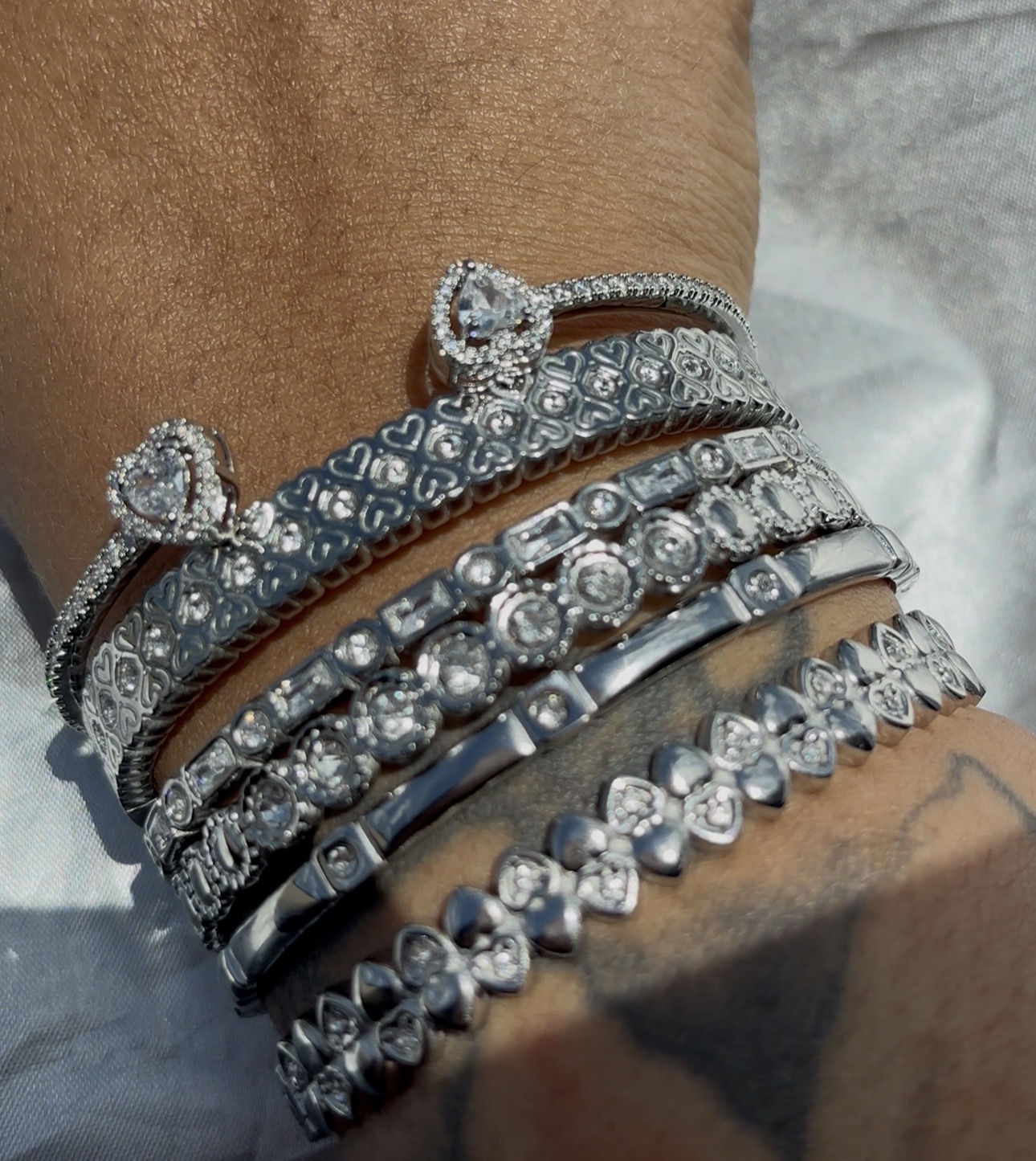Multiple silver bracelets with various designs and gemstones on a person's wrist.