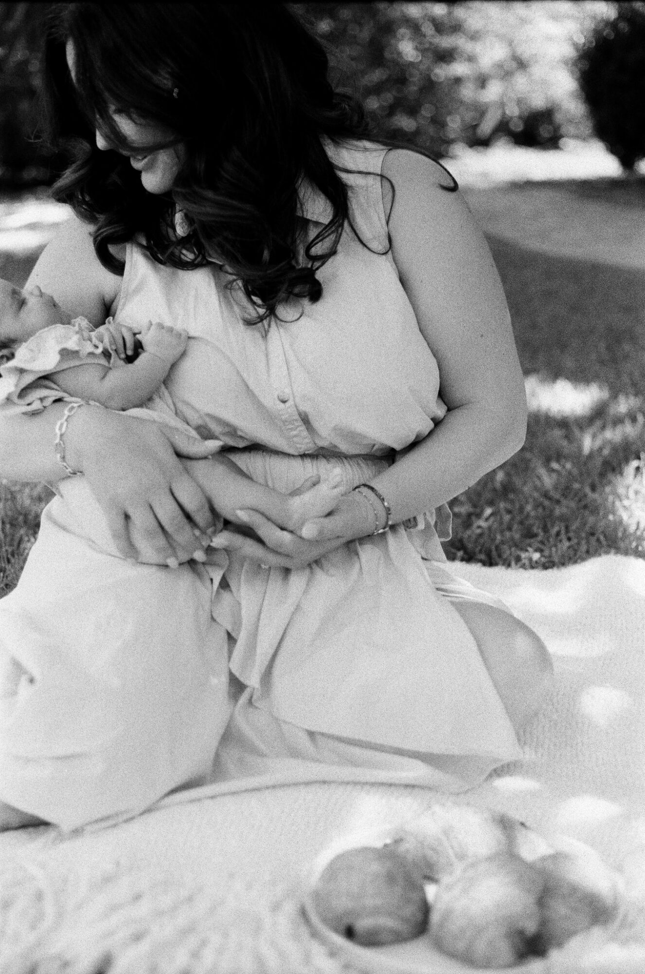 Woman sitting outdoors holding a baby, with three apples on a blanket in front, in black and white.