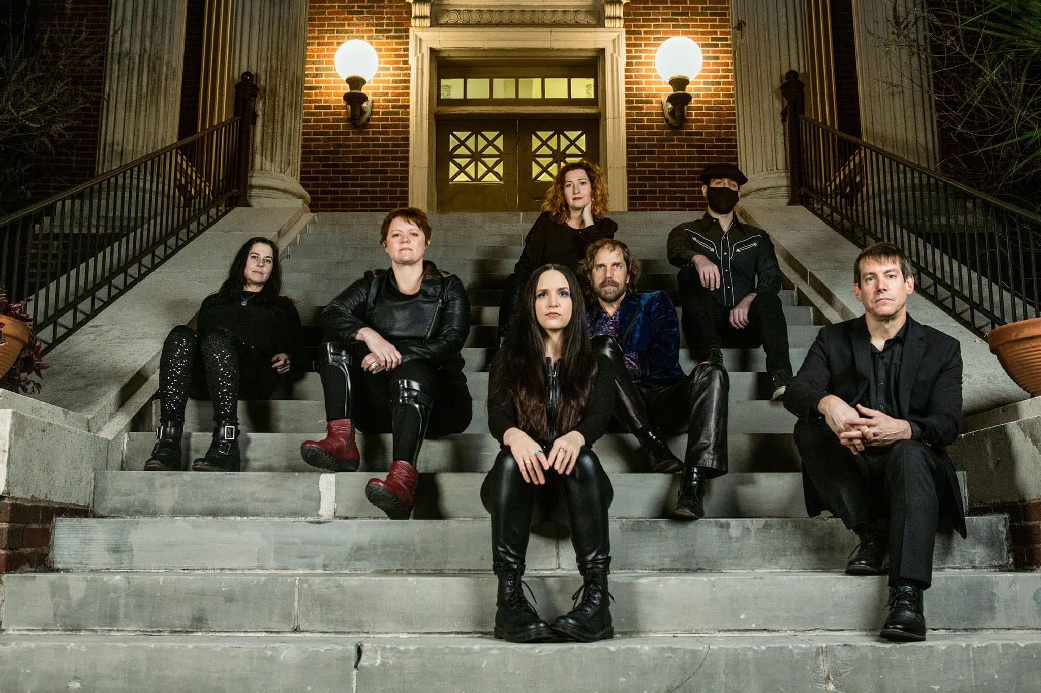 Group of seven people sitting on stairs outside a building with lit lamps, at night.