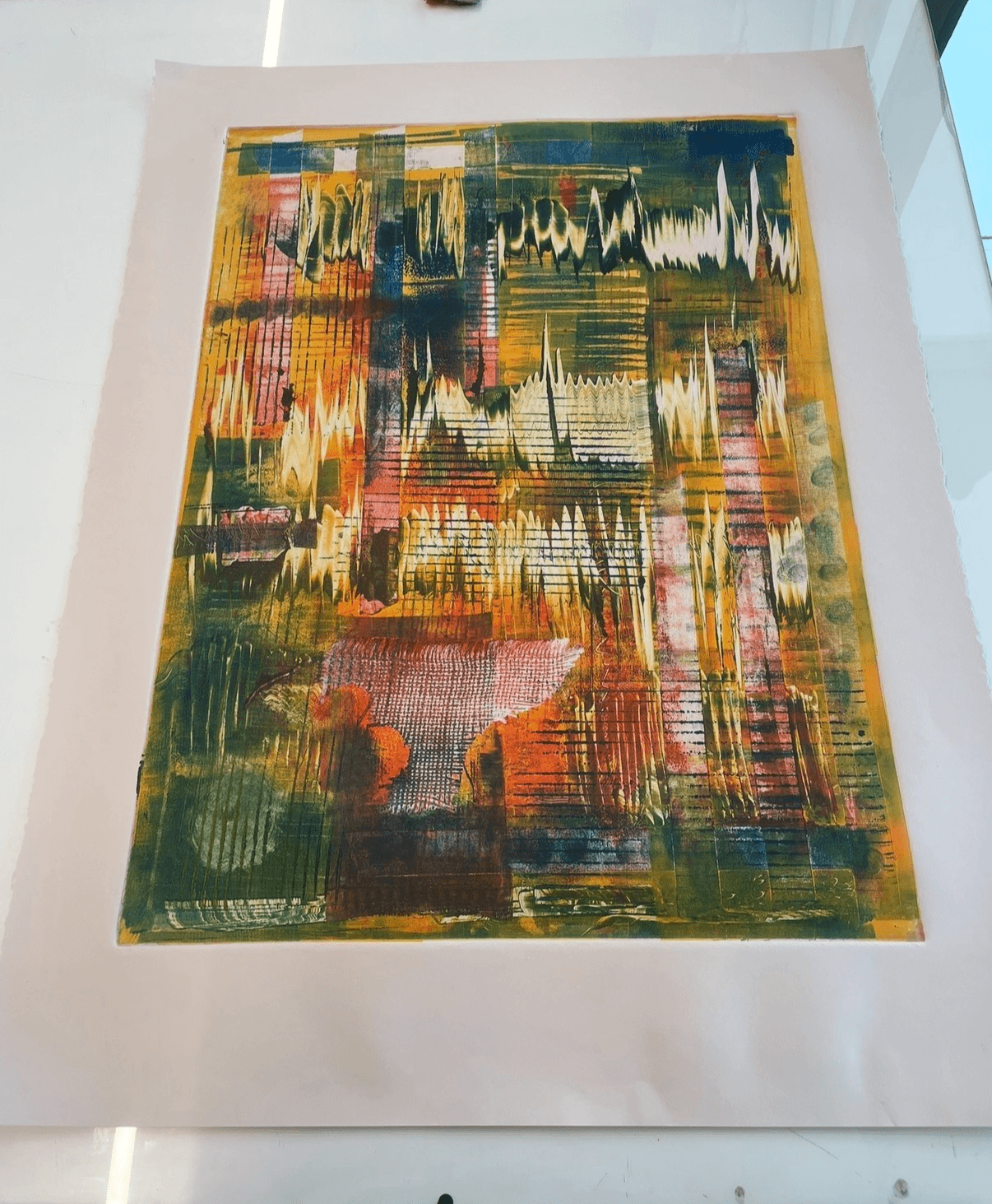 Abstract colorful painting with vertical and horizontal brushstrokes, displayed on a white surface near a window.