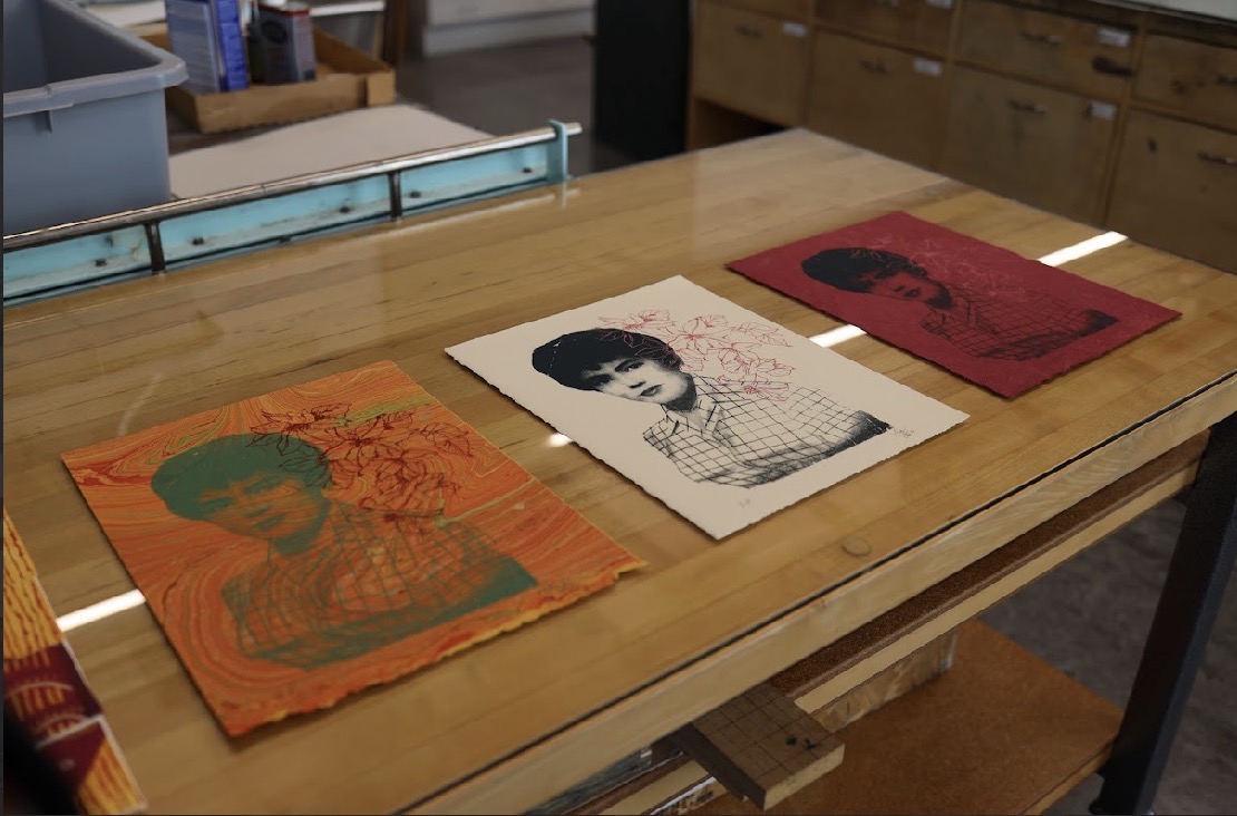 Three vintage-style posters with portraits of women are laid out on a wooden table.