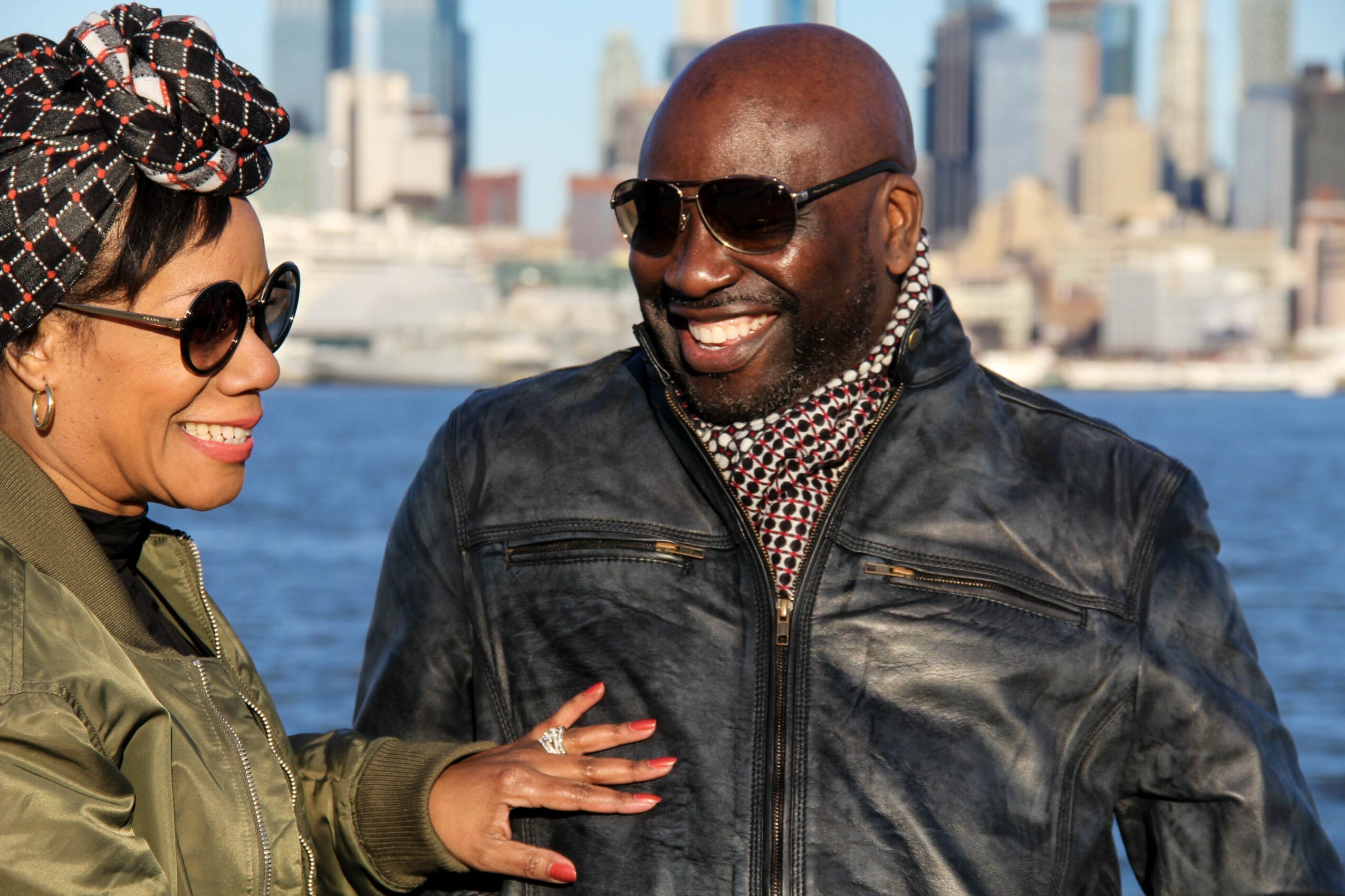 Two people smiling and talking outdoors with a city skyline in the background.